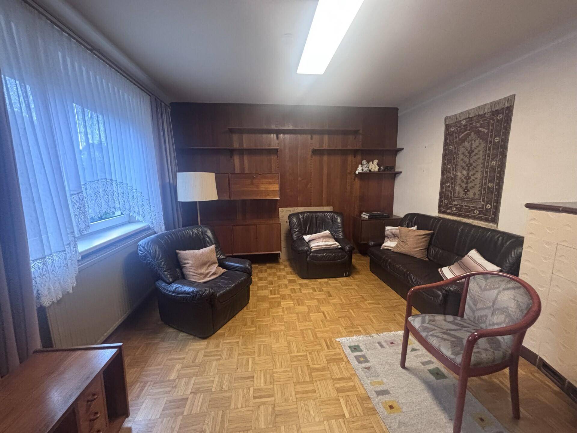 Wohnzimmer mit Parkettboden, dunklen Ledersofas und einer Holzregalwand.