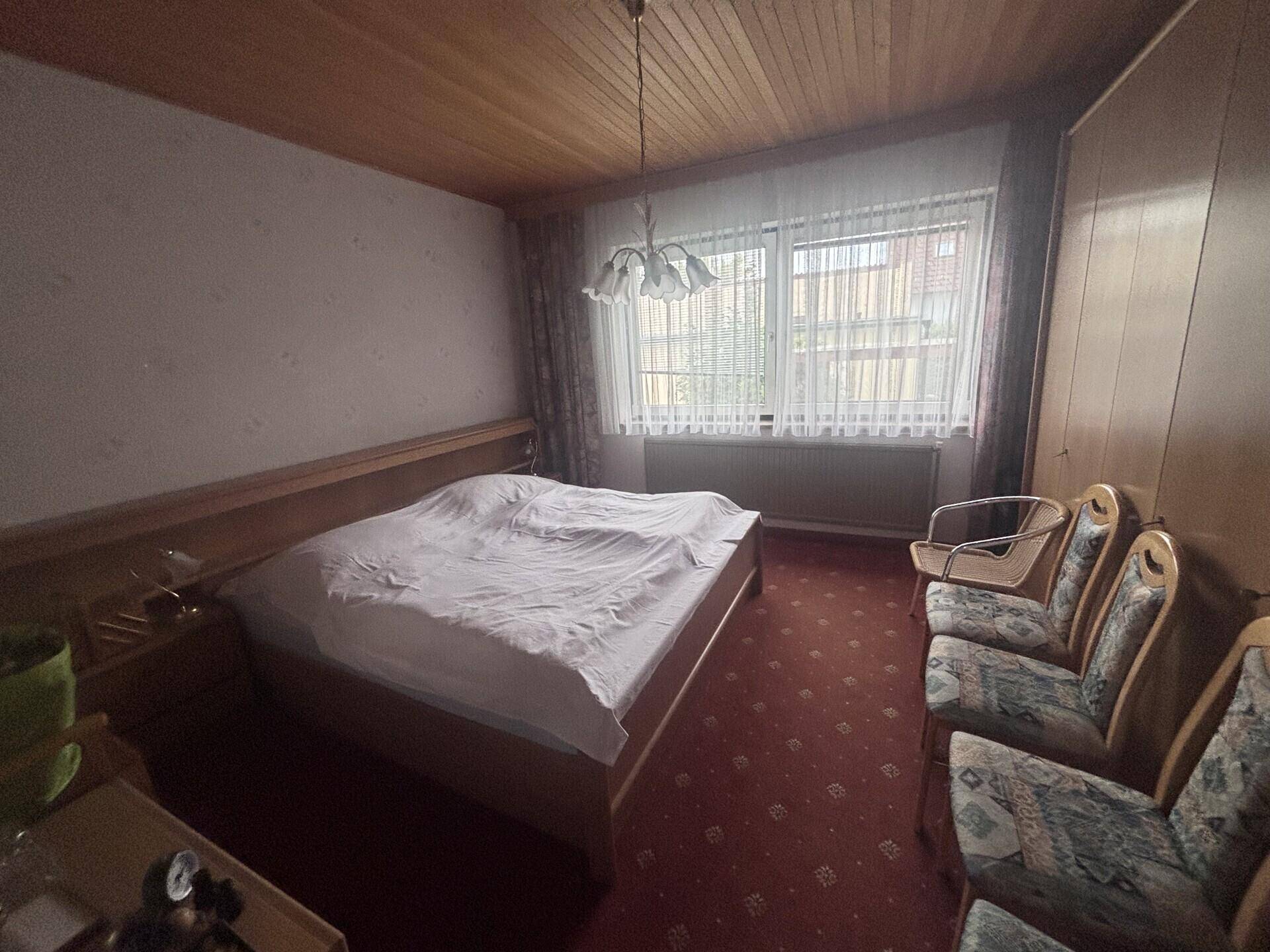 Schlafzimmer mit Doppelbett, Teppichboden und einer Holzdecke, hell durch große Fenster.