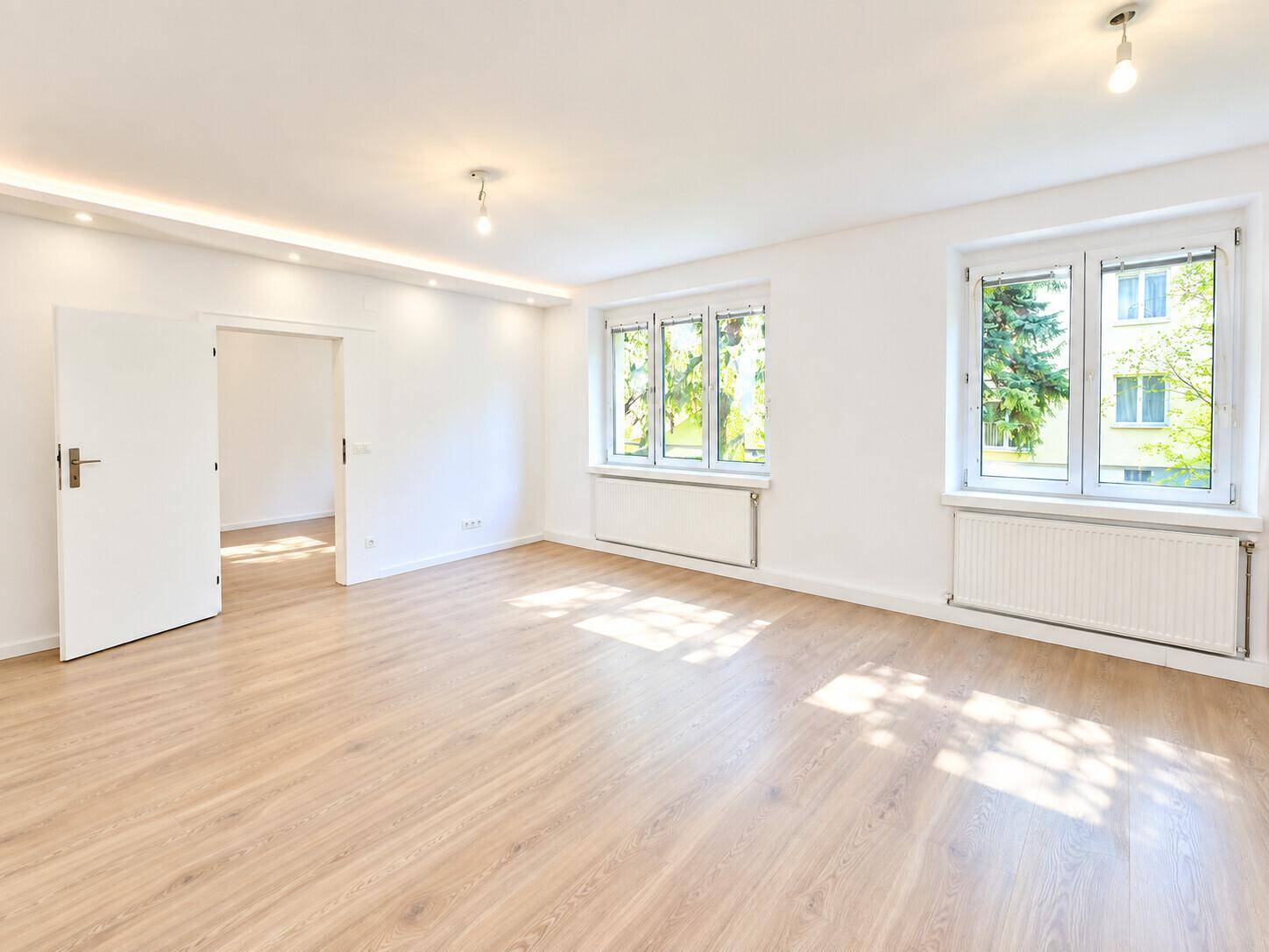 Helles, leeres Wohnzimmer mit modernem Laminatboden und Blick ins Grüne.