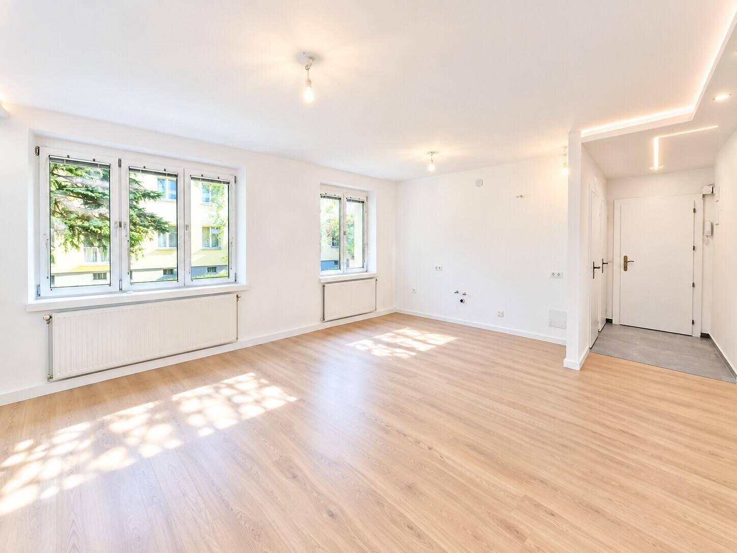 Geräumiges Wohnzimmer mit hellem Laminatboden und Zugang zum Eingangsbereich.