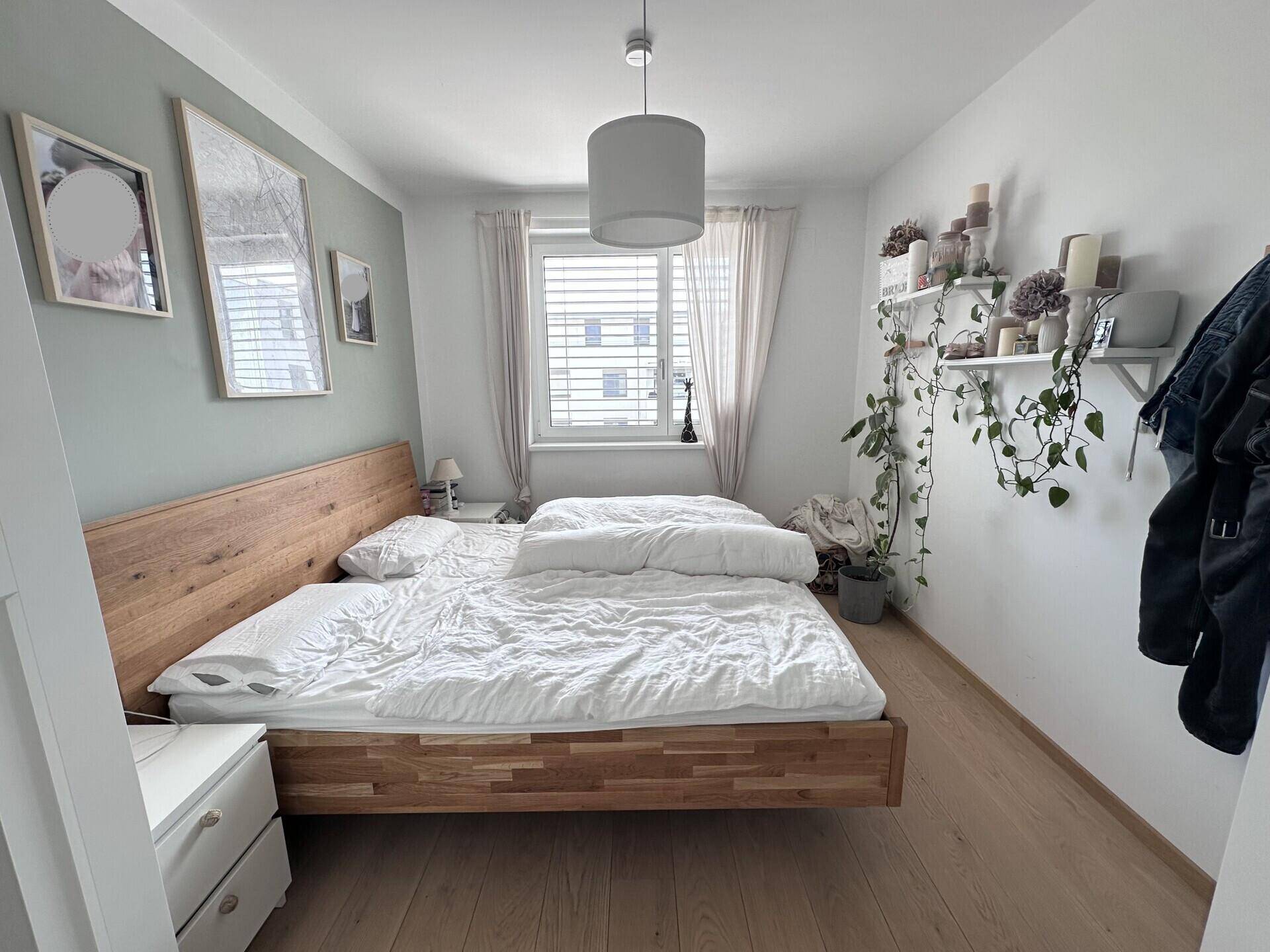 Helles Schlafzimmer mit Holzbett, Parkettboden und Fenster mit Blick ins Grüne.