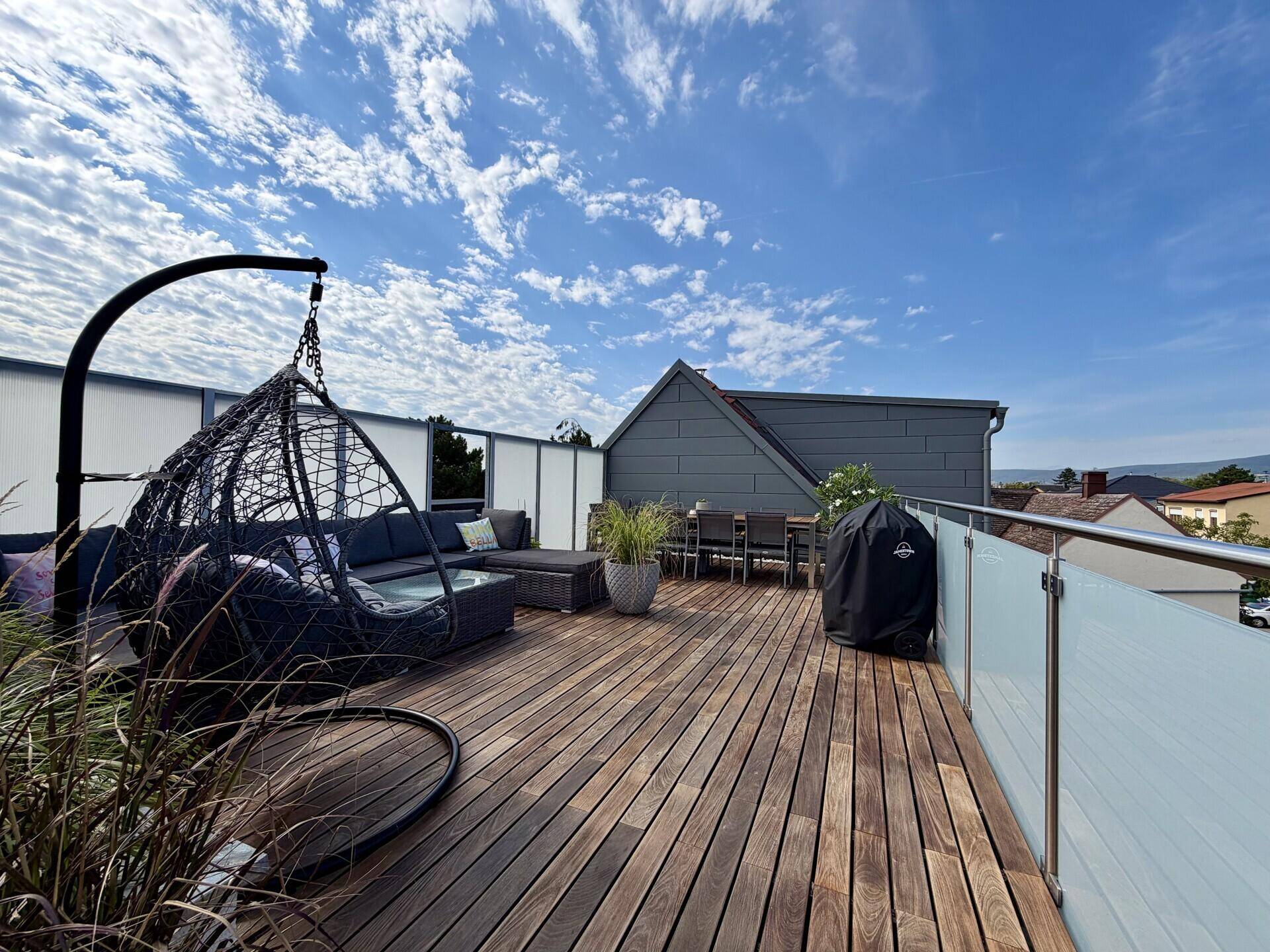 Weitläufige Dachterrasse mit Lounge-Möbeln, Hängesessel und Essbereich unter blauem Himmel.