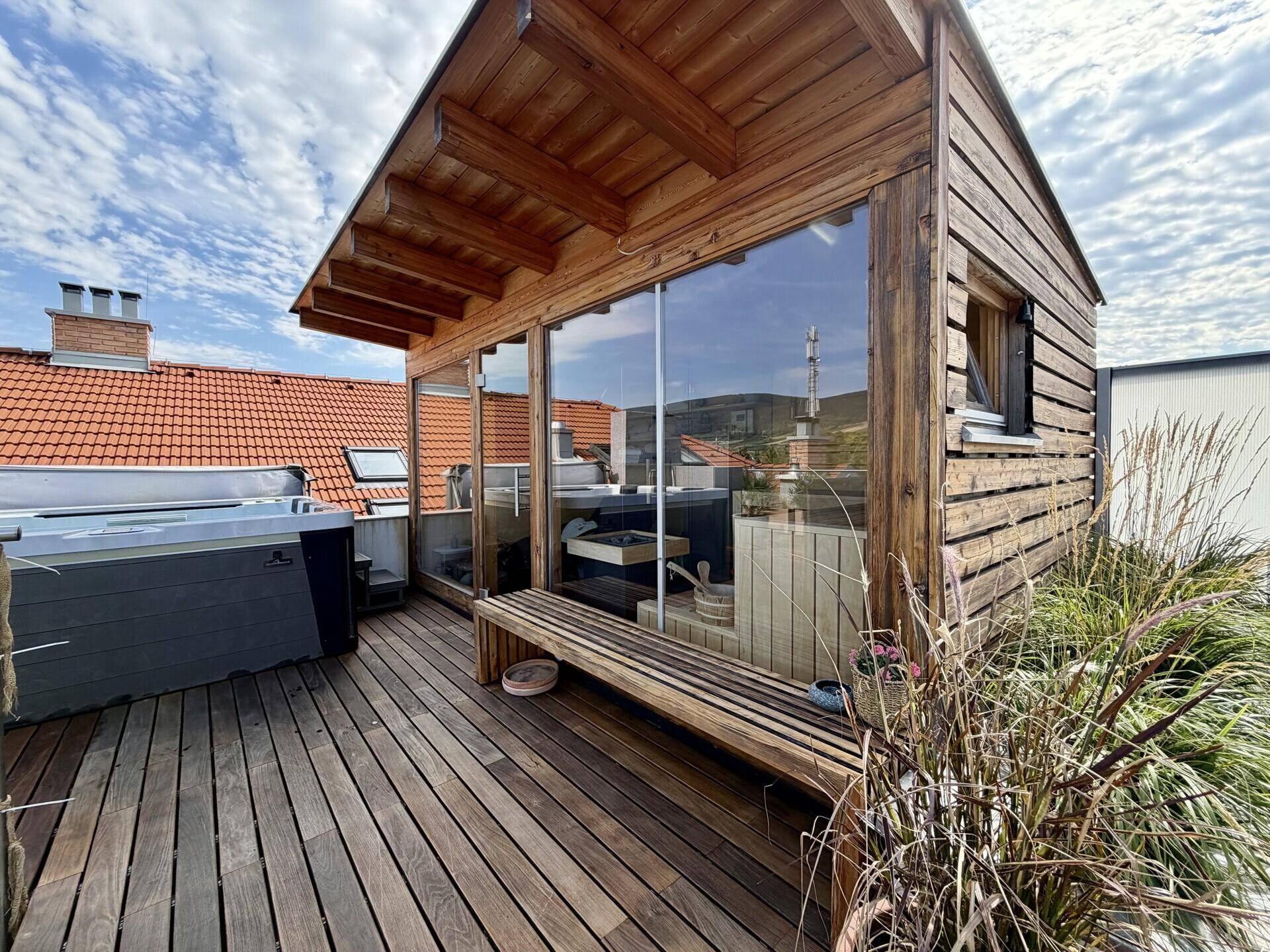 Dachterrasse mit Holzsauna, Whirlpool und Sitzbank, umgeben von Pflanzen und Dächern.