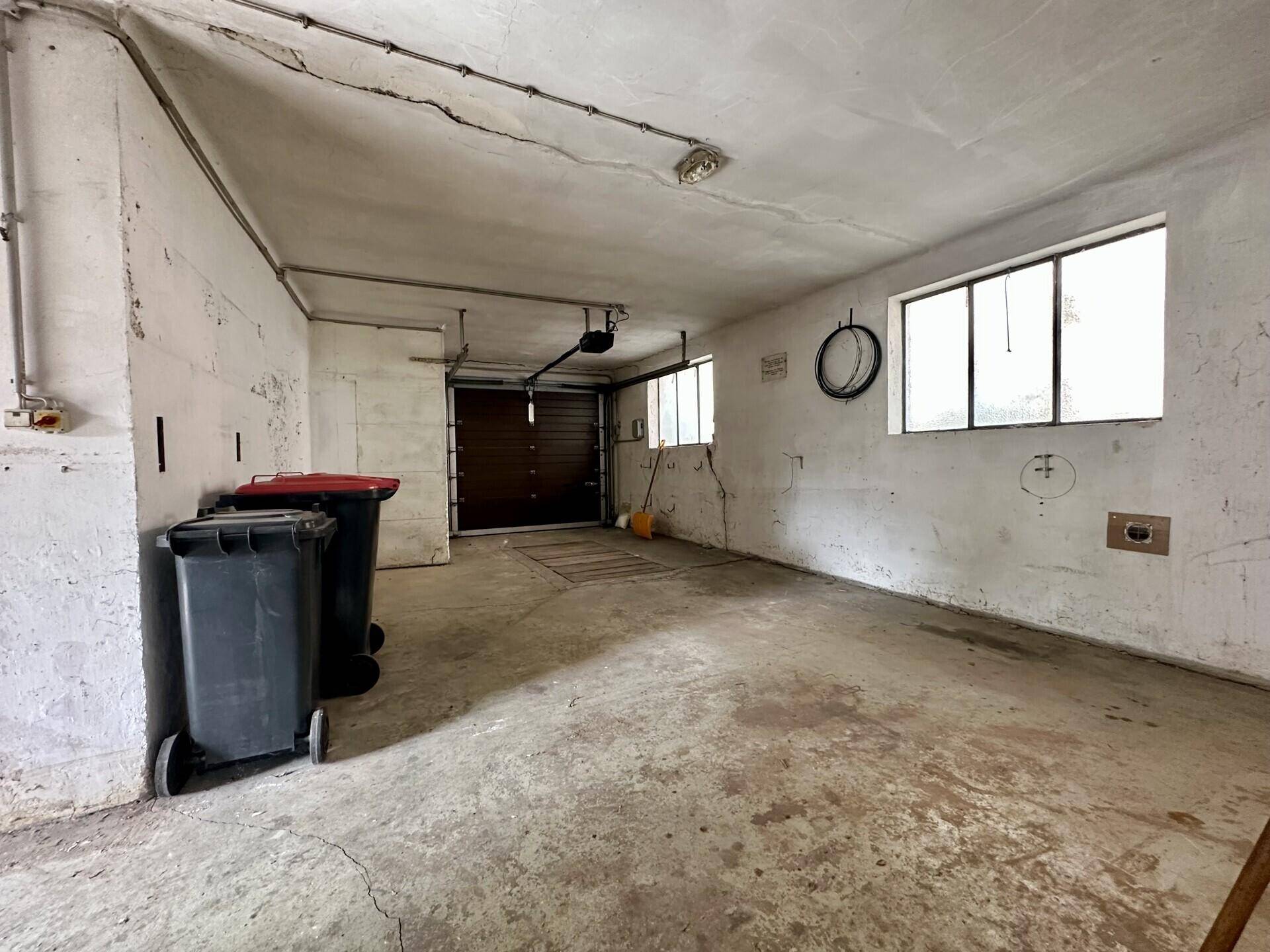 Geräumige Garage mit Betonboden, Rolltor und Fenstern.
