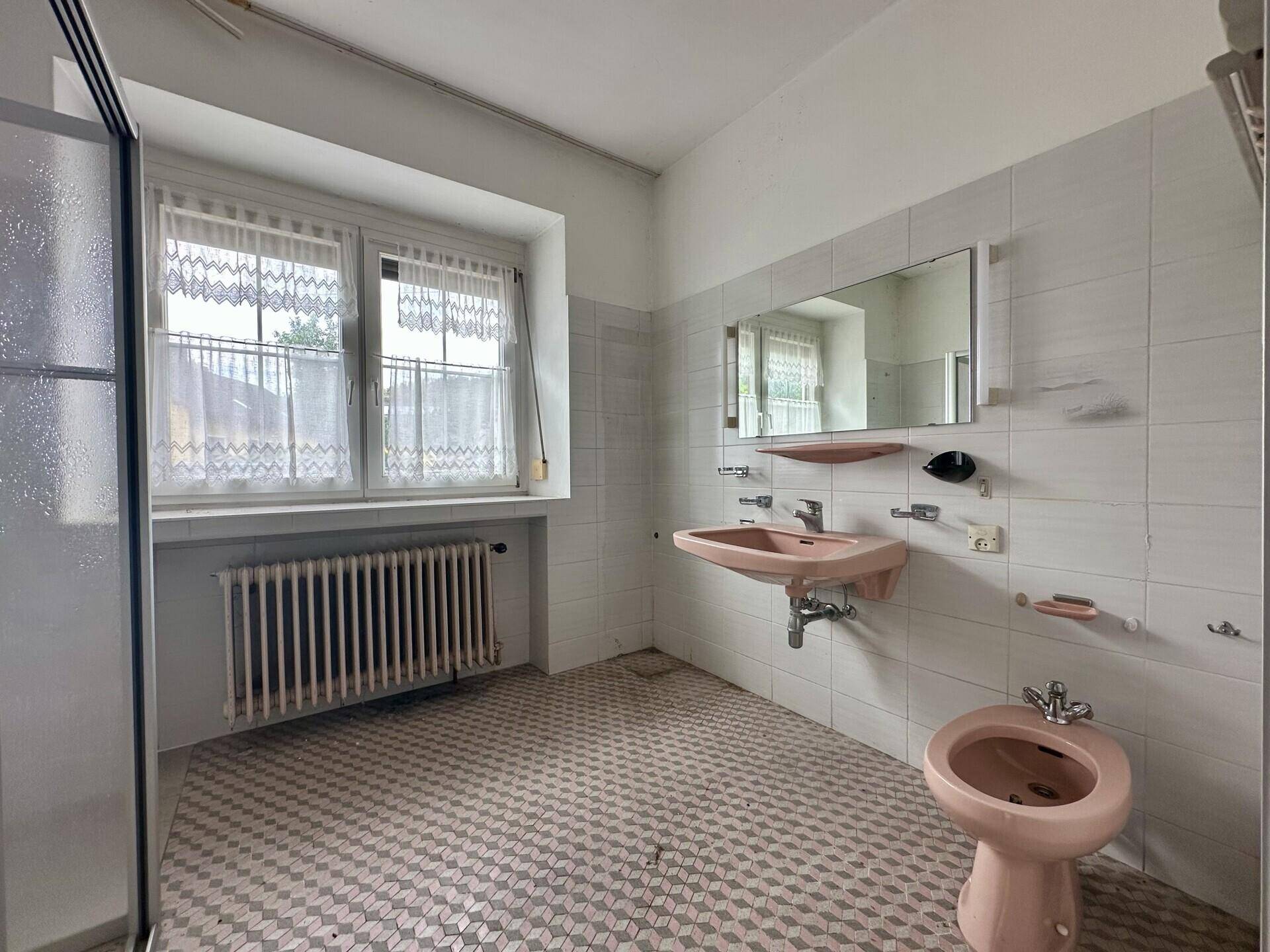 Badezimmer mit rosa Sanitärobjekten, gemusterten Fliesen und Fenster.