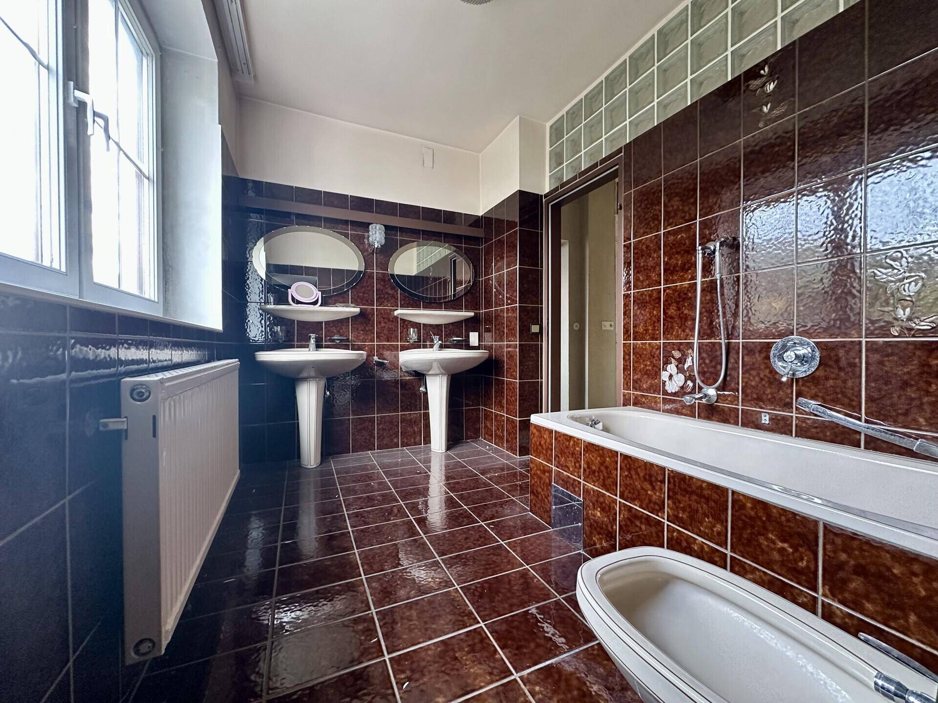 Großes Badezimmer mit braunen Fliesen, Doppelwaschbecken und Badewanne.