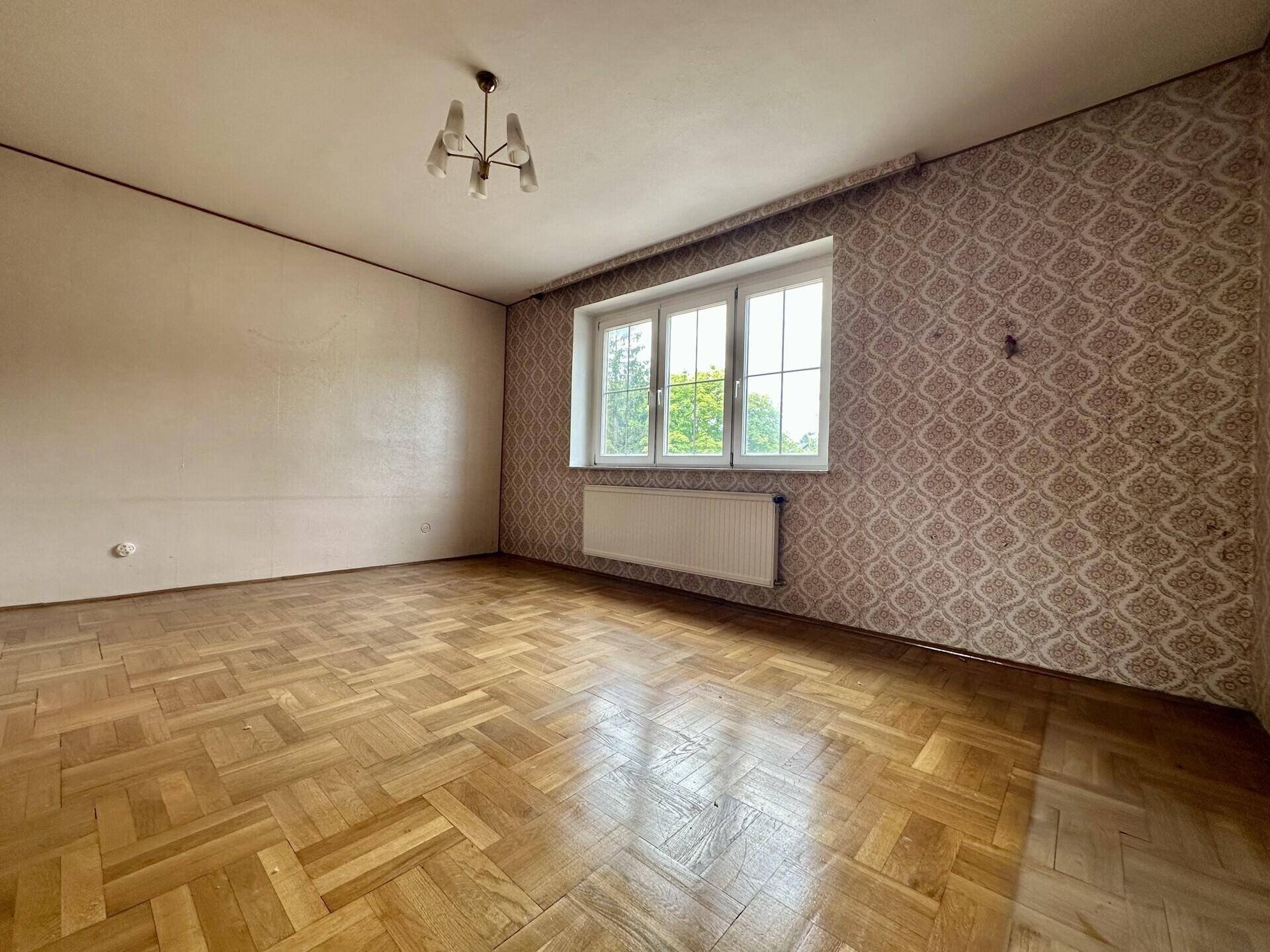 Schlafzimmer mit Parkettboden, gemusterter Tapete und großem Fenster.