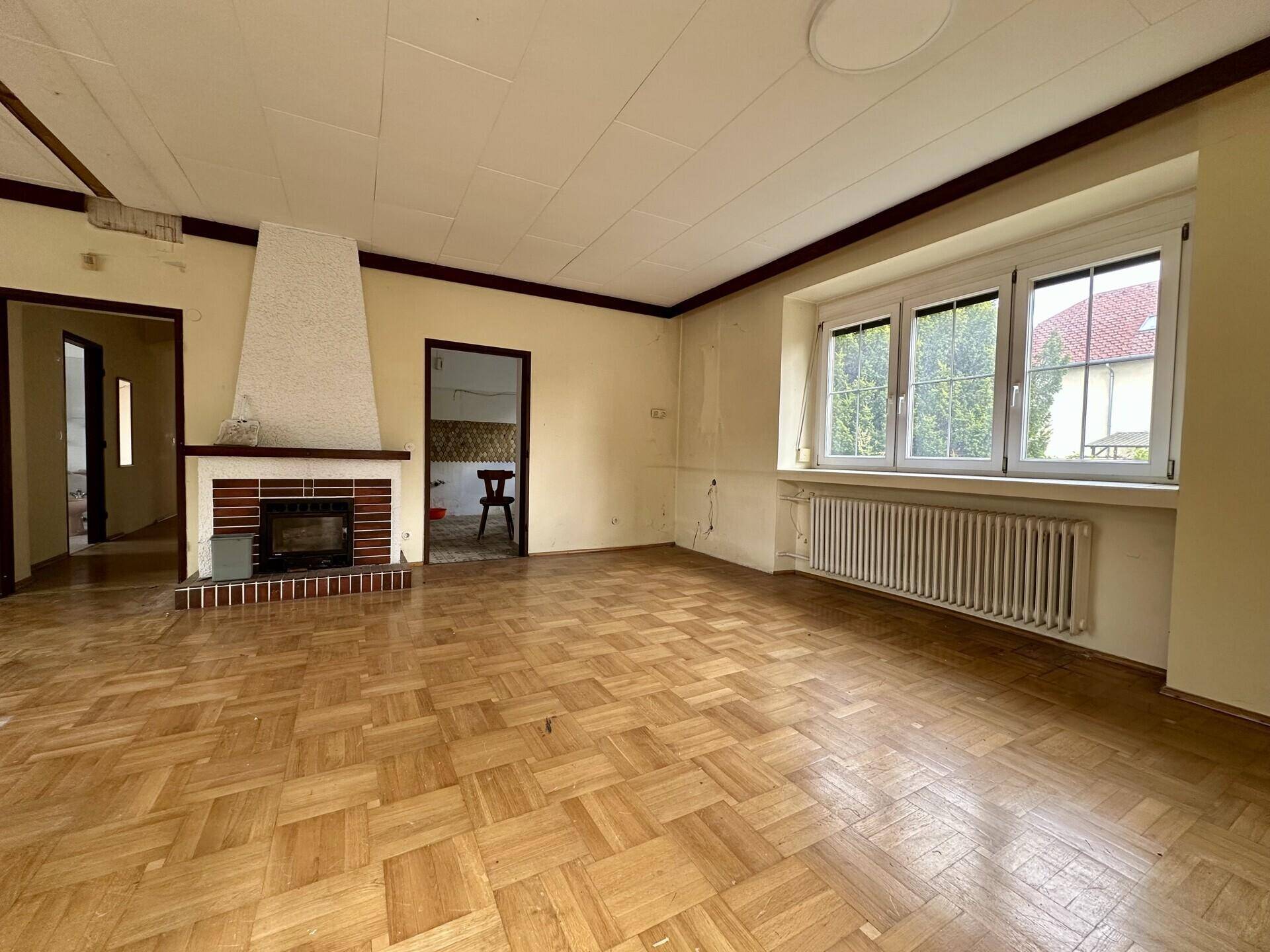 Geräumiges Wohnzimmer mit Fischgrätparkett, Kamin und großen Fenstern.