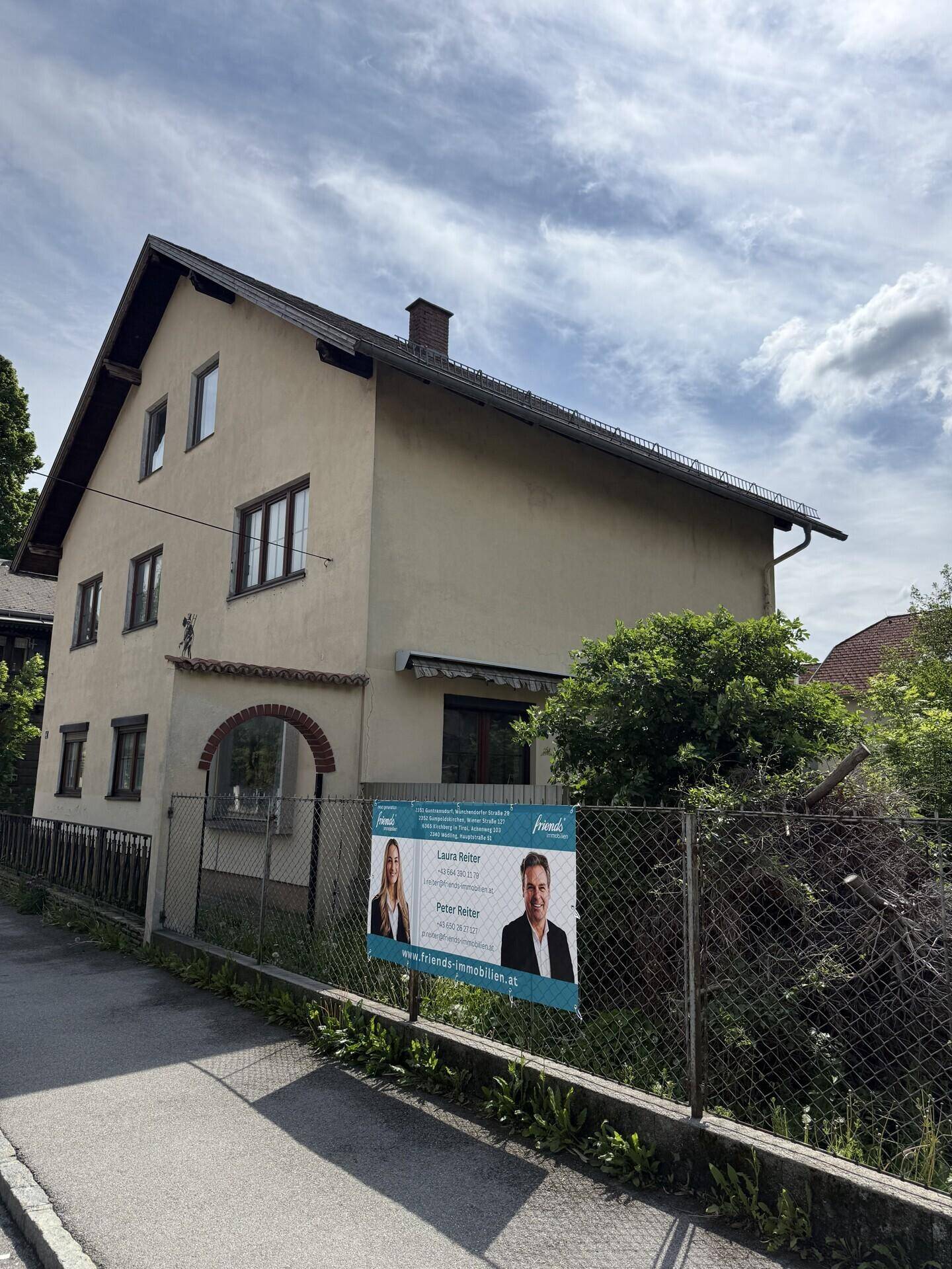 Seitenansicht eines Wohnhauses mit Satteldach und einem Zaun im Vordergrund.