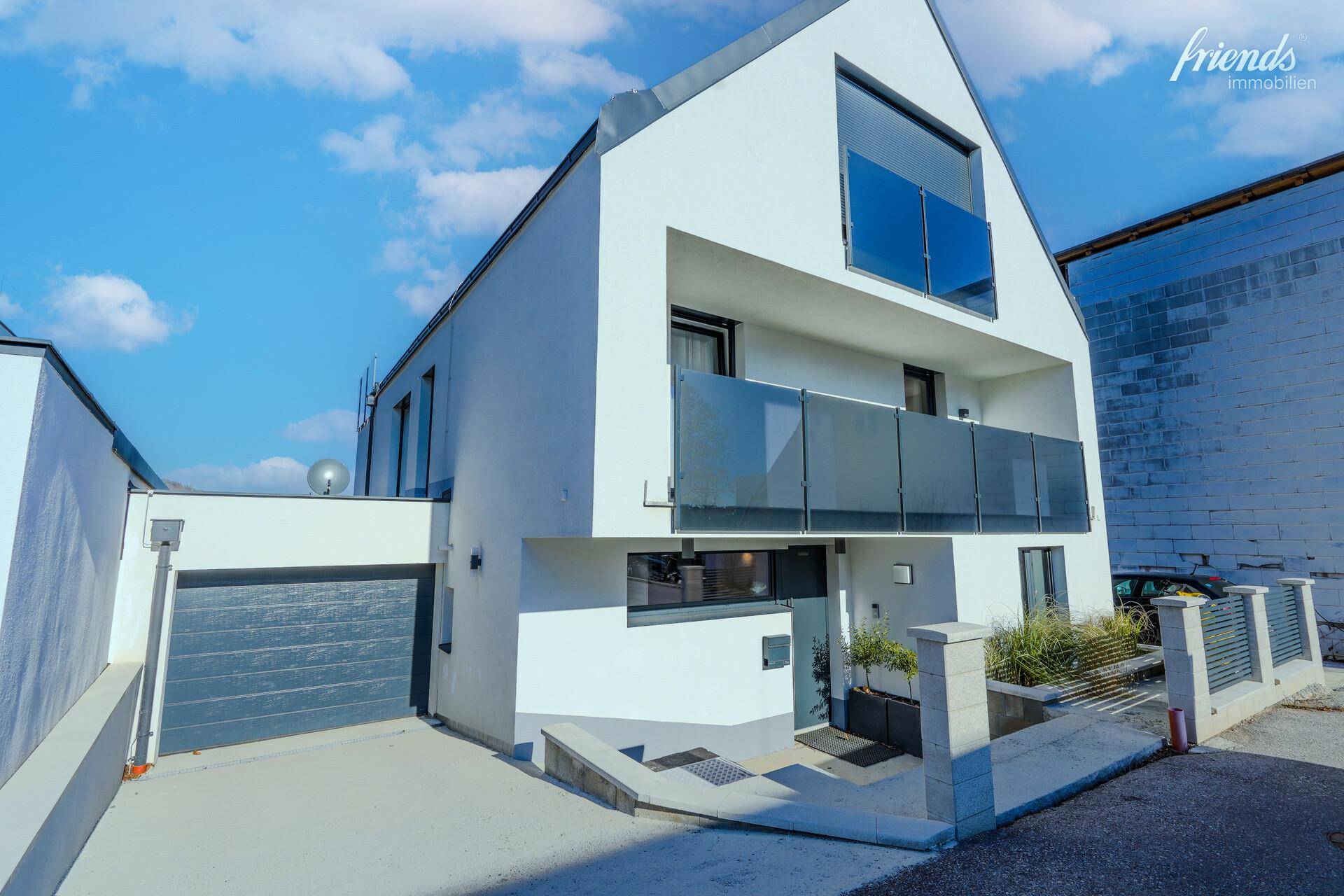 Moderne Hausfassade mit integrierter Garage und Balkonen mit Glasgeländer.