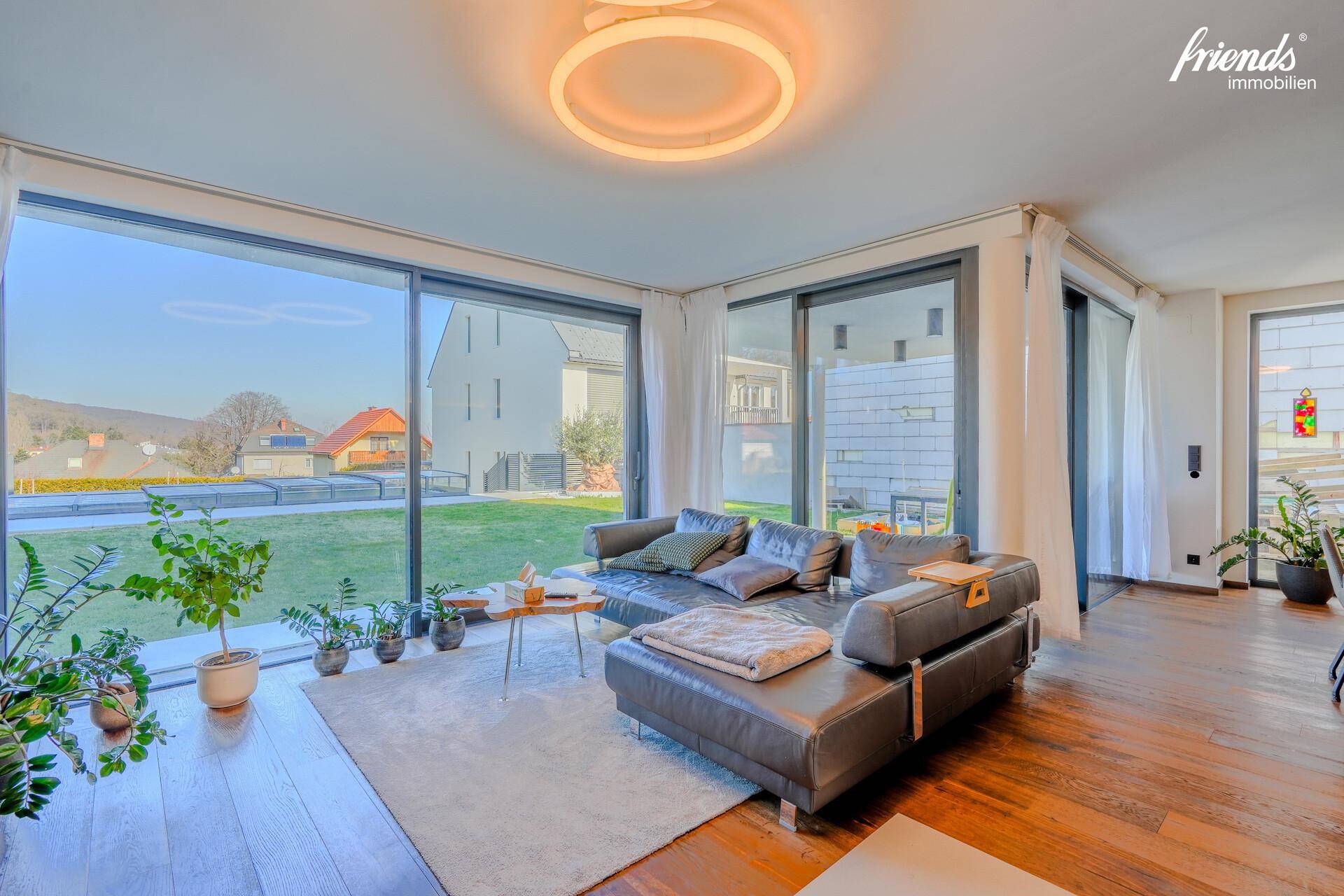 Helles Wohnzimmer mit großen Fenstern, Holzboden und Blick ins Grüne.