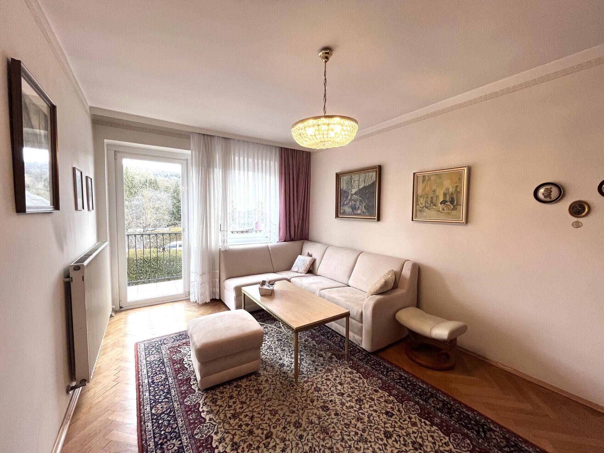 Gemütliches Wohnzimmer mit Parkettboden, Sofa und Zugang zu einem kleinen Balkon.