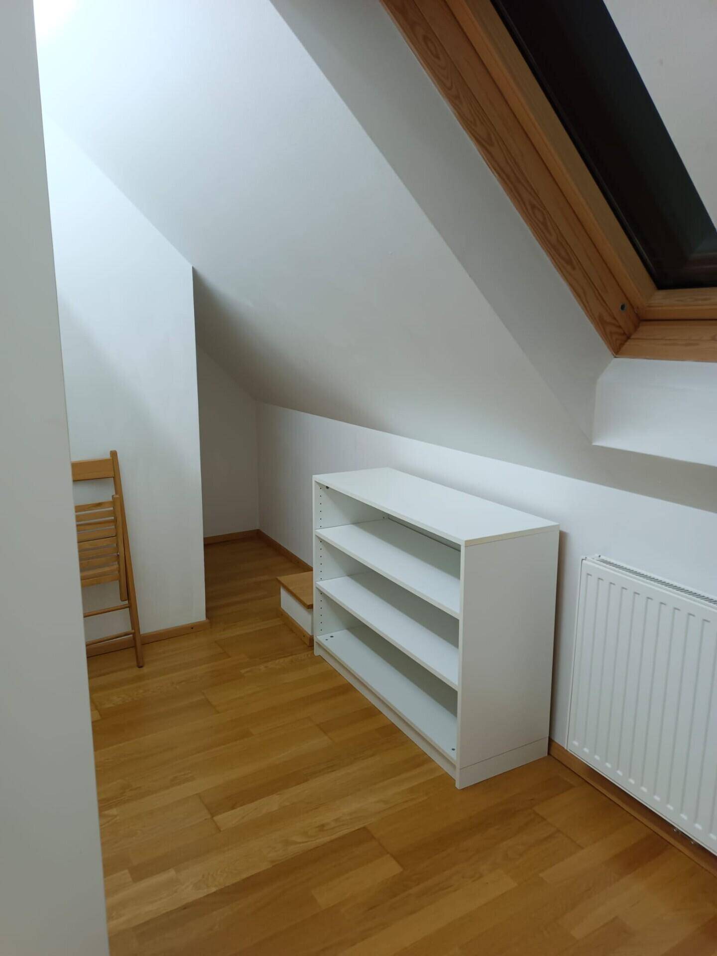 Dachgeschossraum mit Holzparkett, weißem Regal und einem Dachfenster für natürliches Licht.