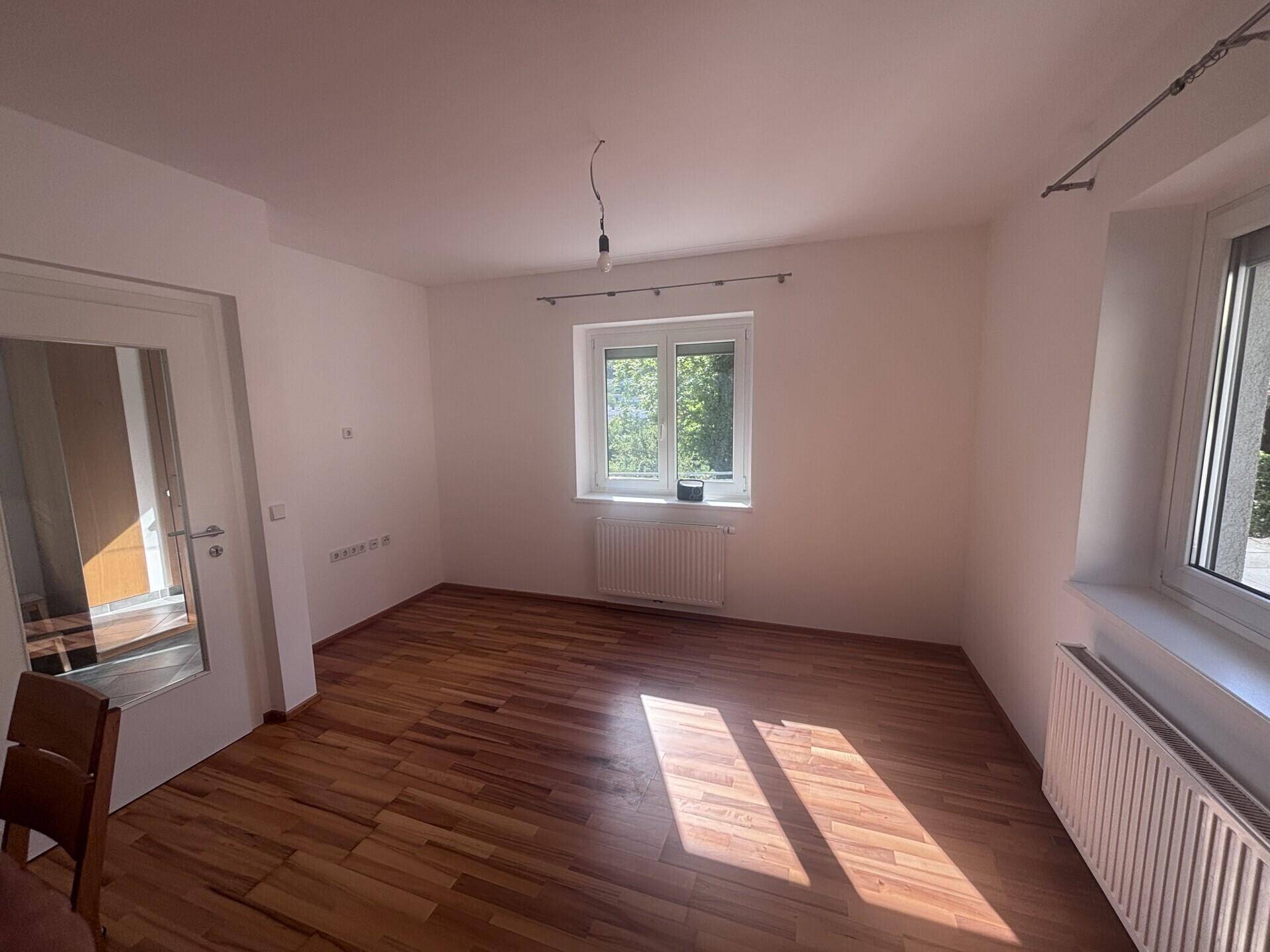 Geräumiger Raum mit Holzparkettboden, weißen Wänden und viel natürlichem Licht durch die Fenster.