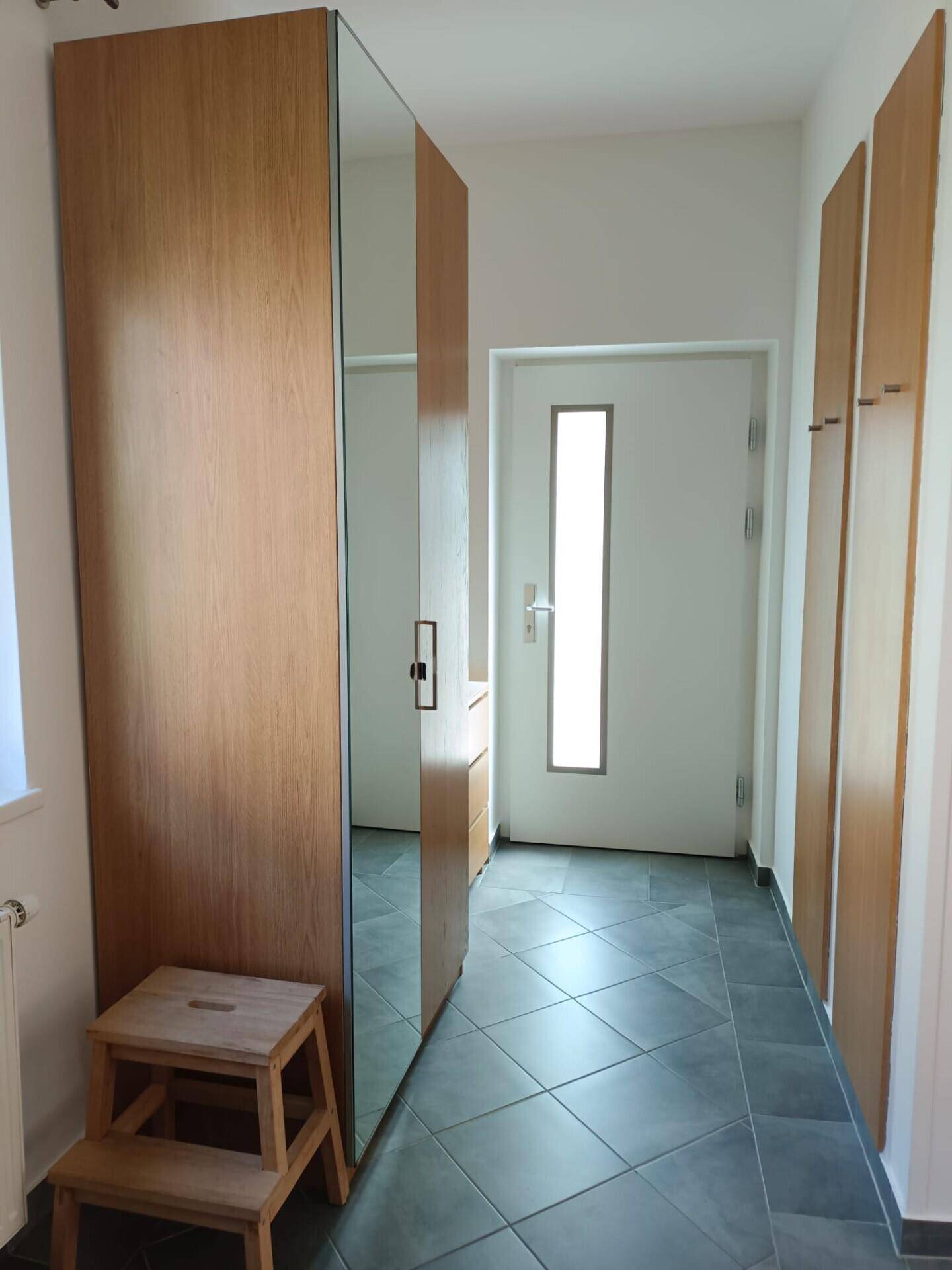 Eingangsbereich mit Fliesenboden, Holzschränken und einer modernen Eingangstür mit Glaseinsatz.