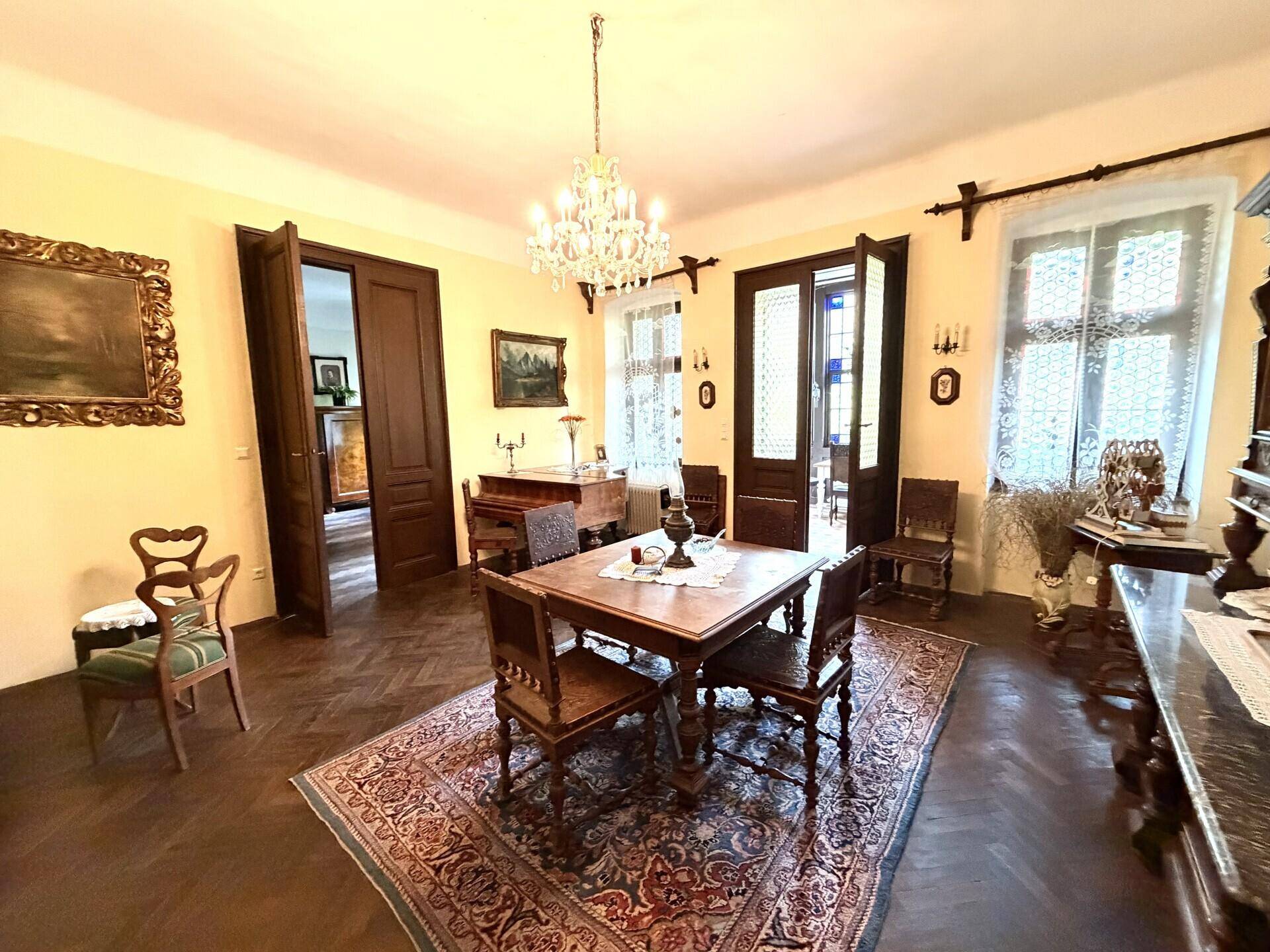 Elegantes Esszimmer mit antiken Möbeln, Fischgrätparkett und einem prächtigen Kronleuchter, der den Raum erhellt.