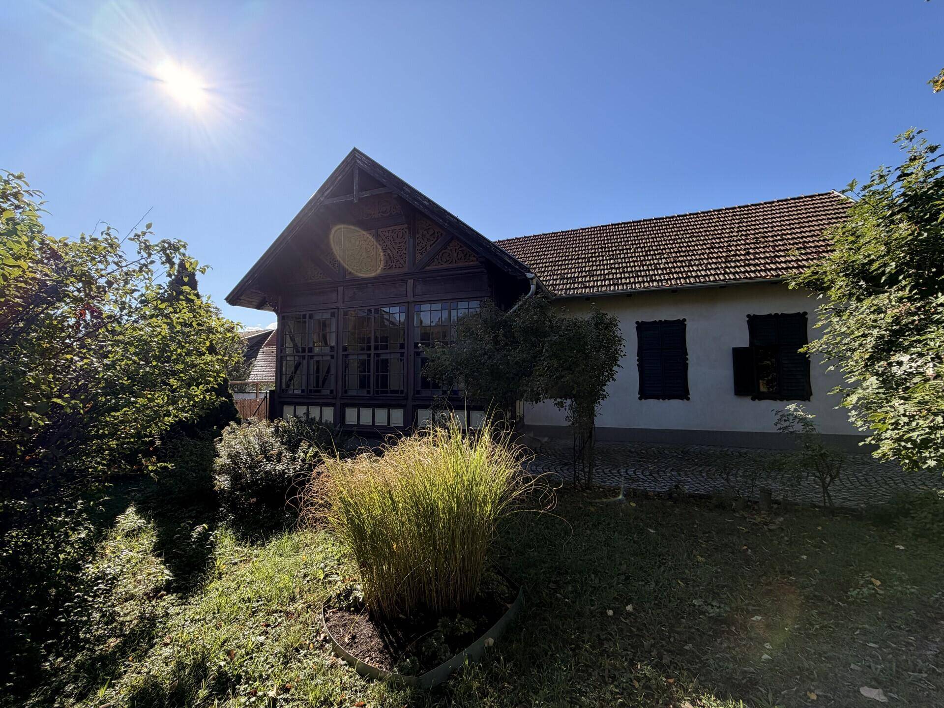 Sonniges Anwesen mit einem historischen Gebäude und üppiger Vegetation, umgeben von Natur unter klarem Himmel.