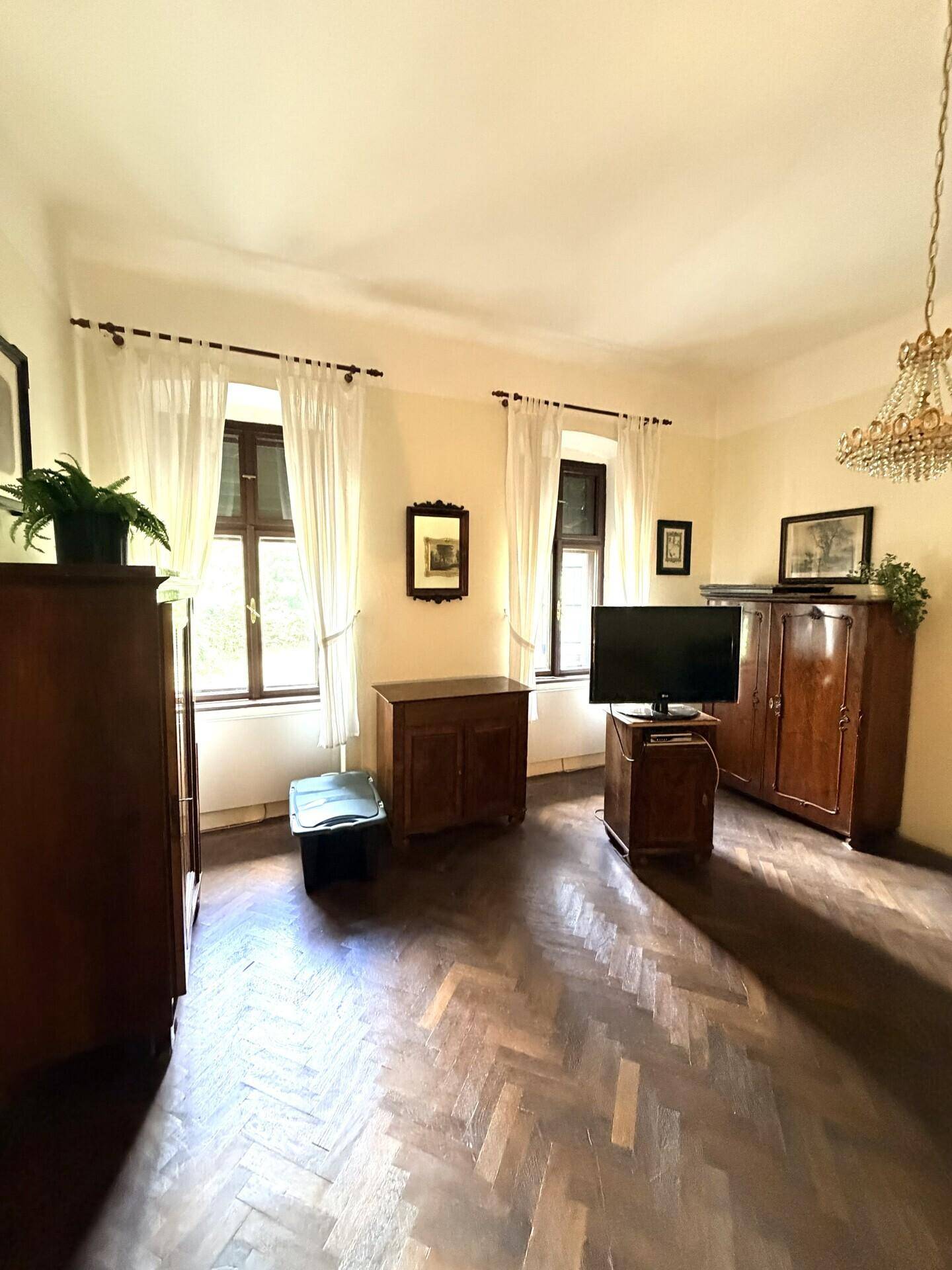 Helles Schlafzimmer mit klassischem Interieur, dunklem Fischgrätparkett und zwei Fenstern für viel Tageslicht.