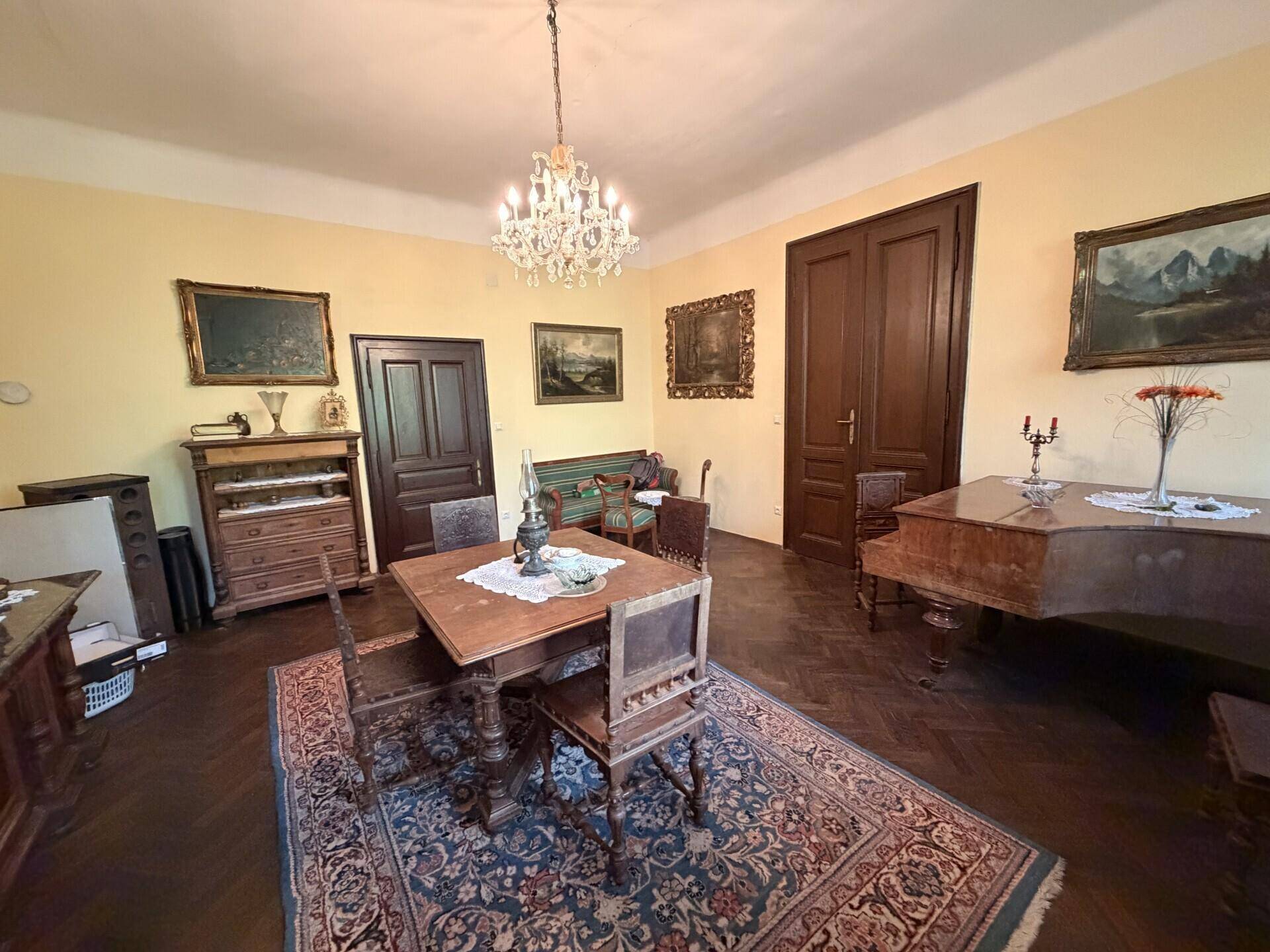 Geräumiges Esszimmer mit klassischem Interieur, dunklem Holzparkett und einem antiken Klavier, das zum Verweilen einlädt.