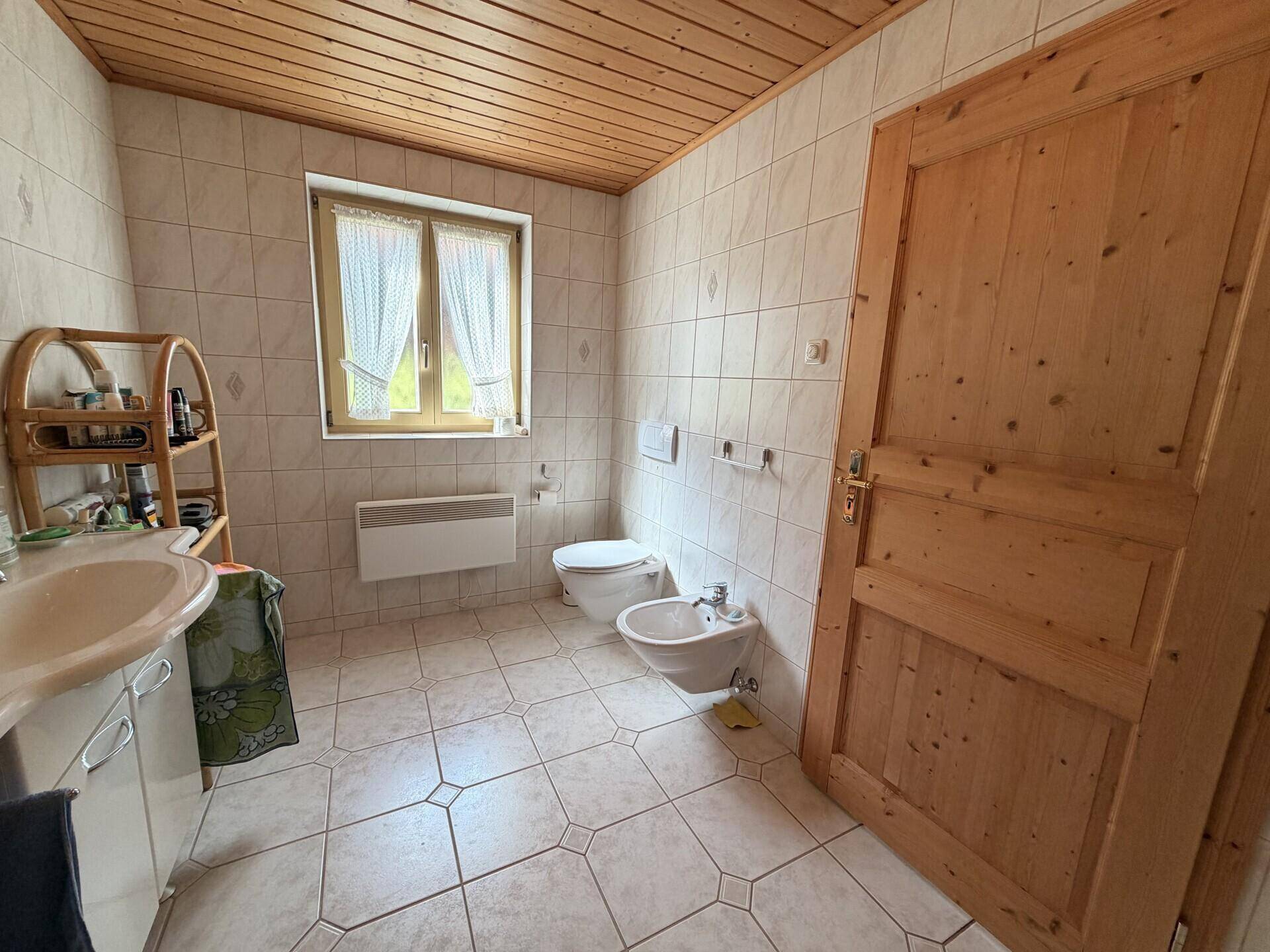 Funktionales Badezimmer mit Fliesenboden, Holzdecke und einer Holztür, die den Raum abgrenzt.