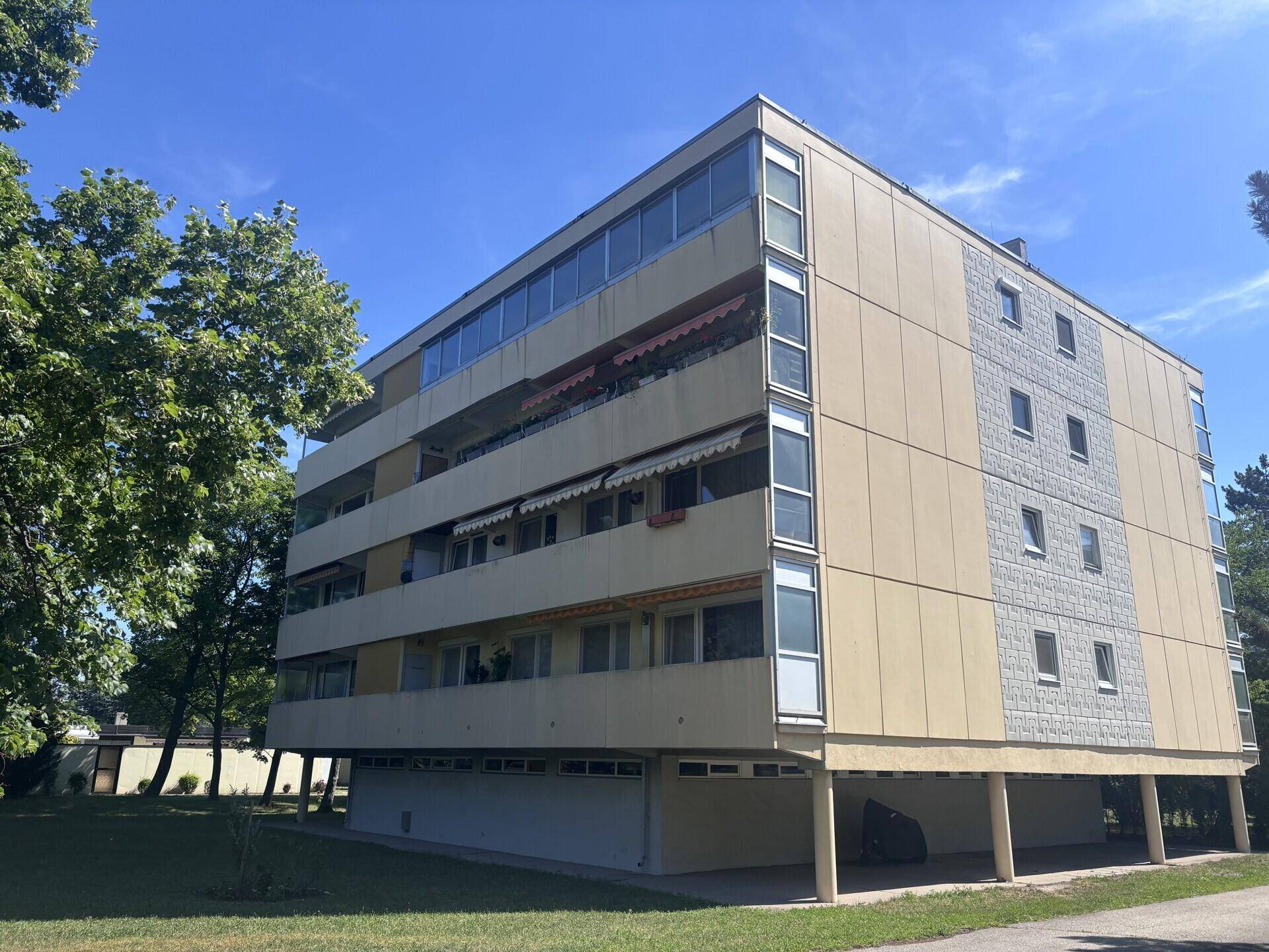 Mehrstöckiges Apartmentgebäude mit beiger Fassade, großen Fenstern und verglasten Balkonen.