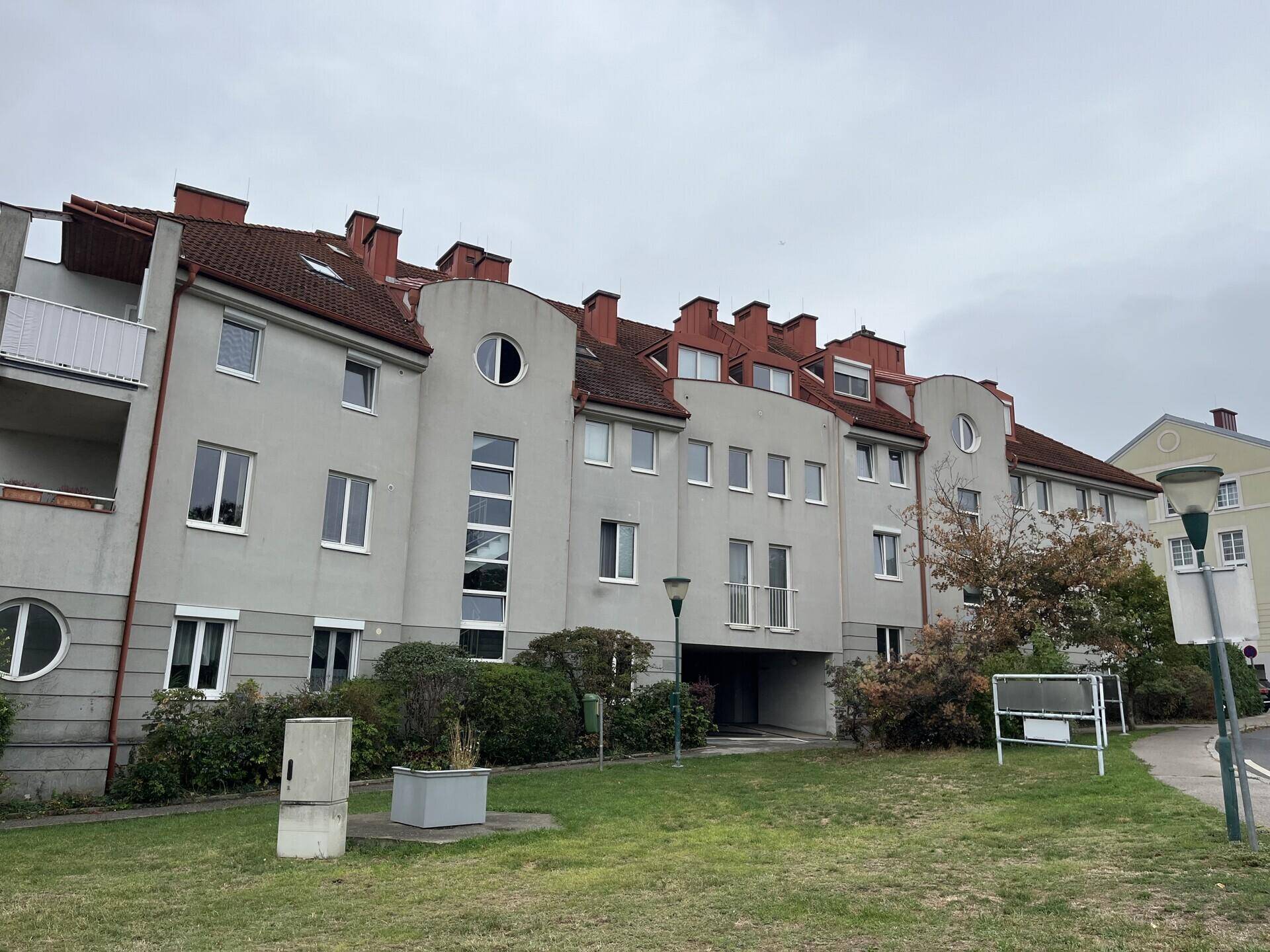 Ansicht der Gebäudefassade mit mehreren Fenstern und Grünflächen im Vordergrund.