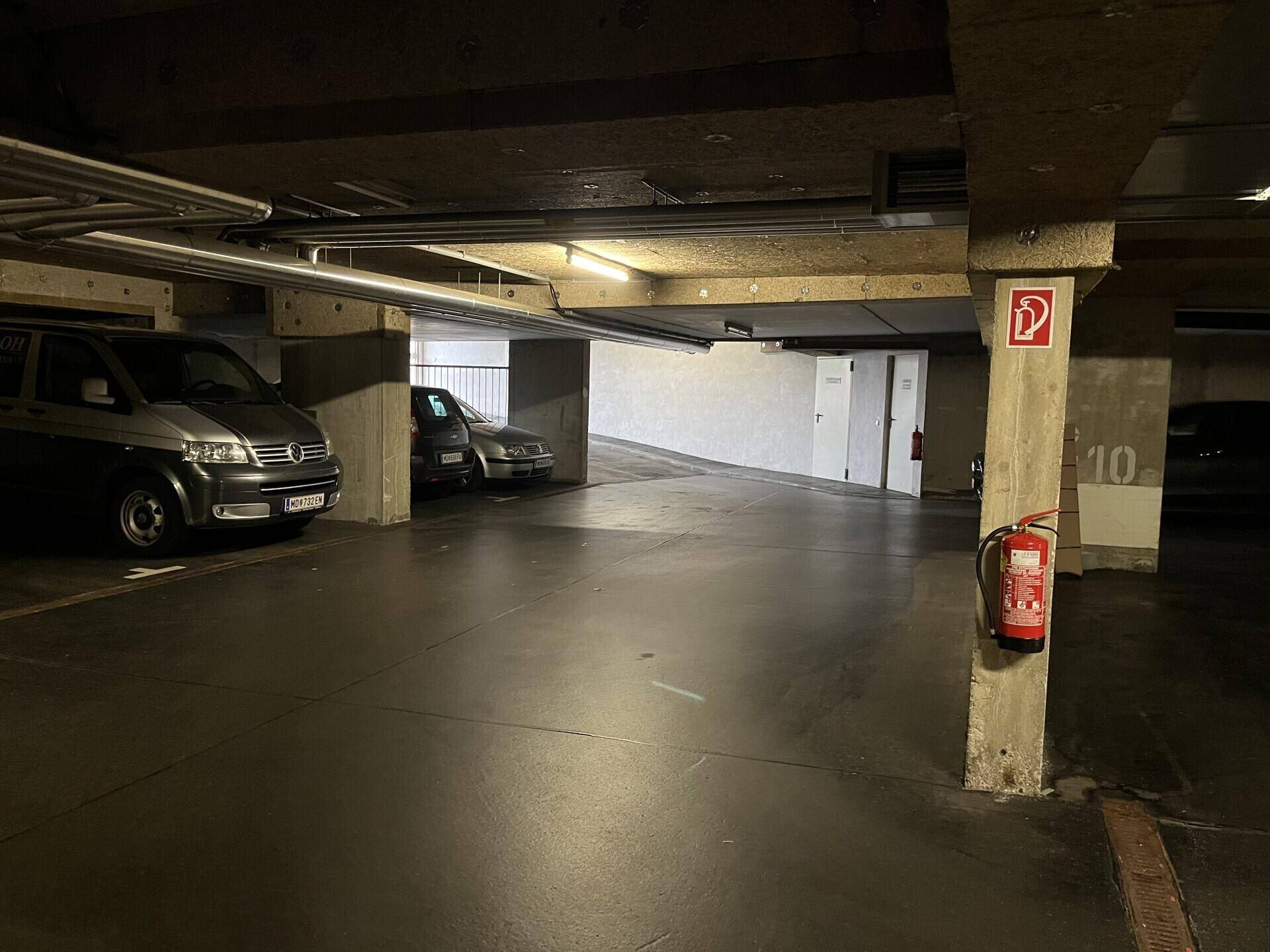 Geräumige Tiefgarage mit mehreren geparkten Fahrzeugen und Zufahrtsrampe.