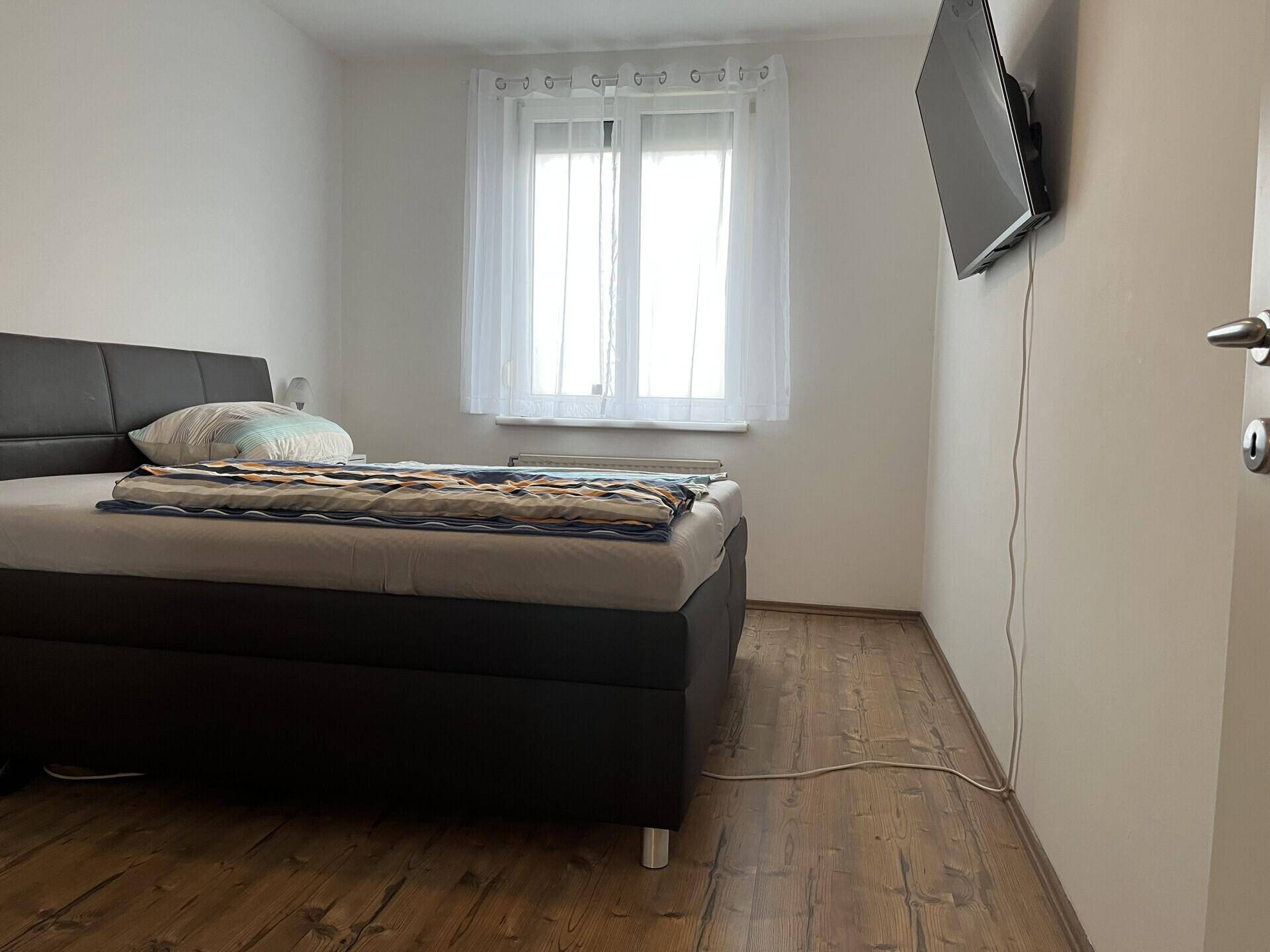 Schlafzimmer mit Doppelbett und an der Wand montiertem Fernseher, mit Holzboden.