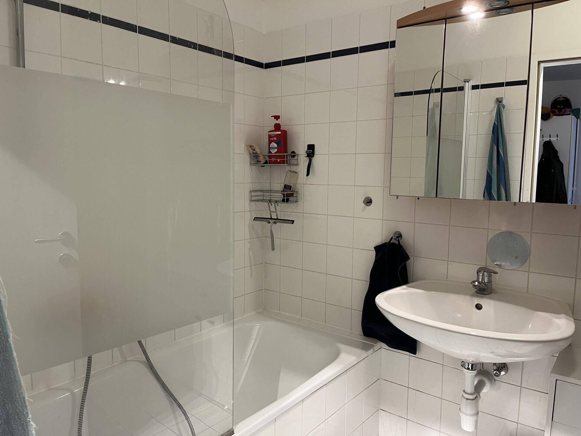 Badezimmer mit Badewanne, Duschabtrennung, Waschbecken und Spiegelschrank, komplett gefliest.