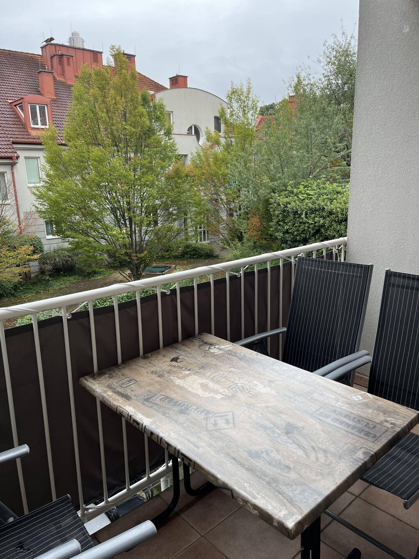 Balkon mit Sitzgelegenheiten und Blick auf die grüne Umgebung und andere Gebäude.