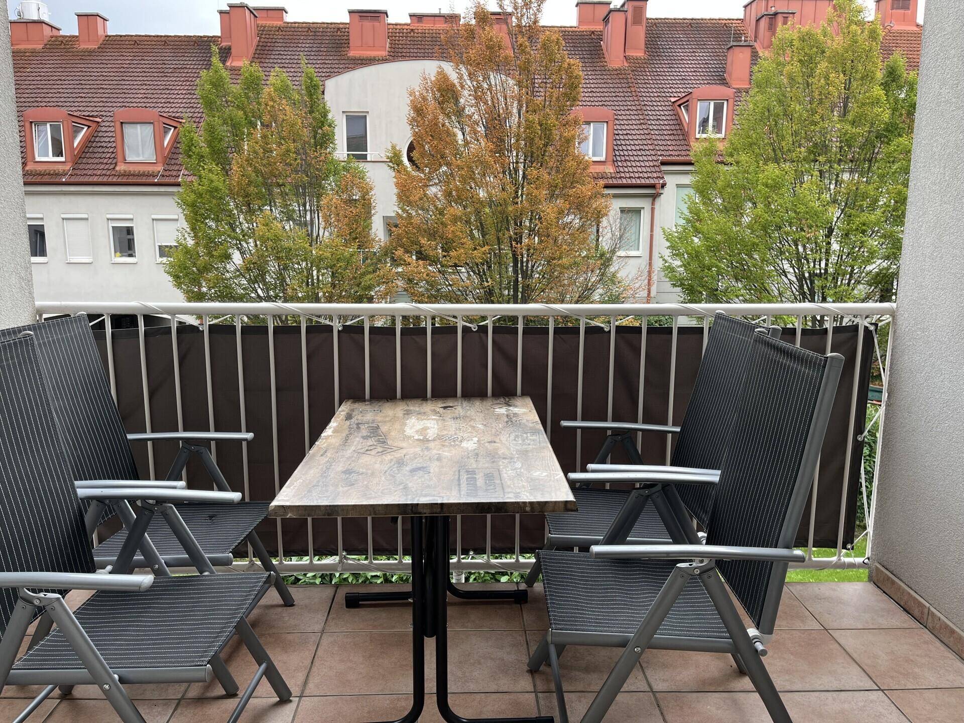 Gemütlicher Balkon mit Terrassenmöbeln und Blick auf die umliegenden Gebäude und Bäume.
