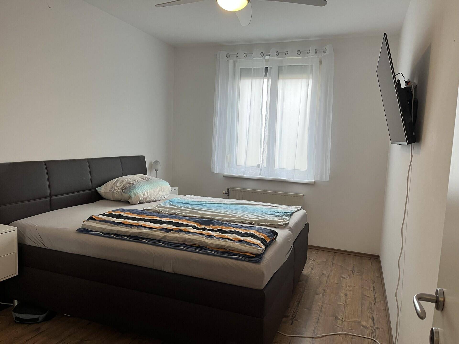 Schlafzimmer mit Doppelbett, Fenster und Deckenventilator, ausgestattet mit Holzboden.