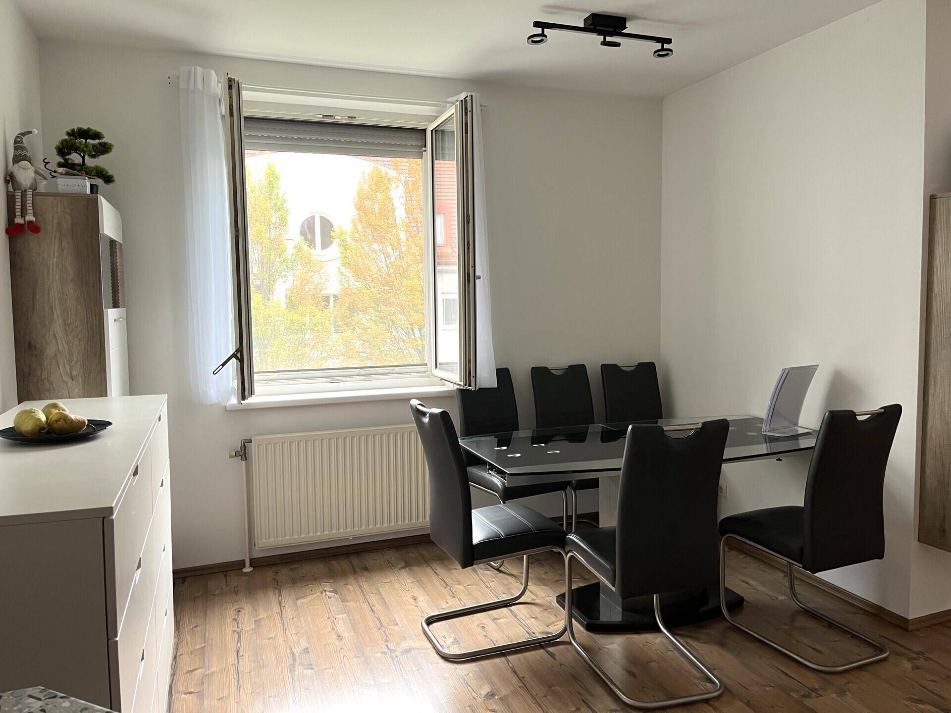 Heller Essbereich mit modernem Glastisch und schwarzen Stühlen, direkt am Fenster gelegen.