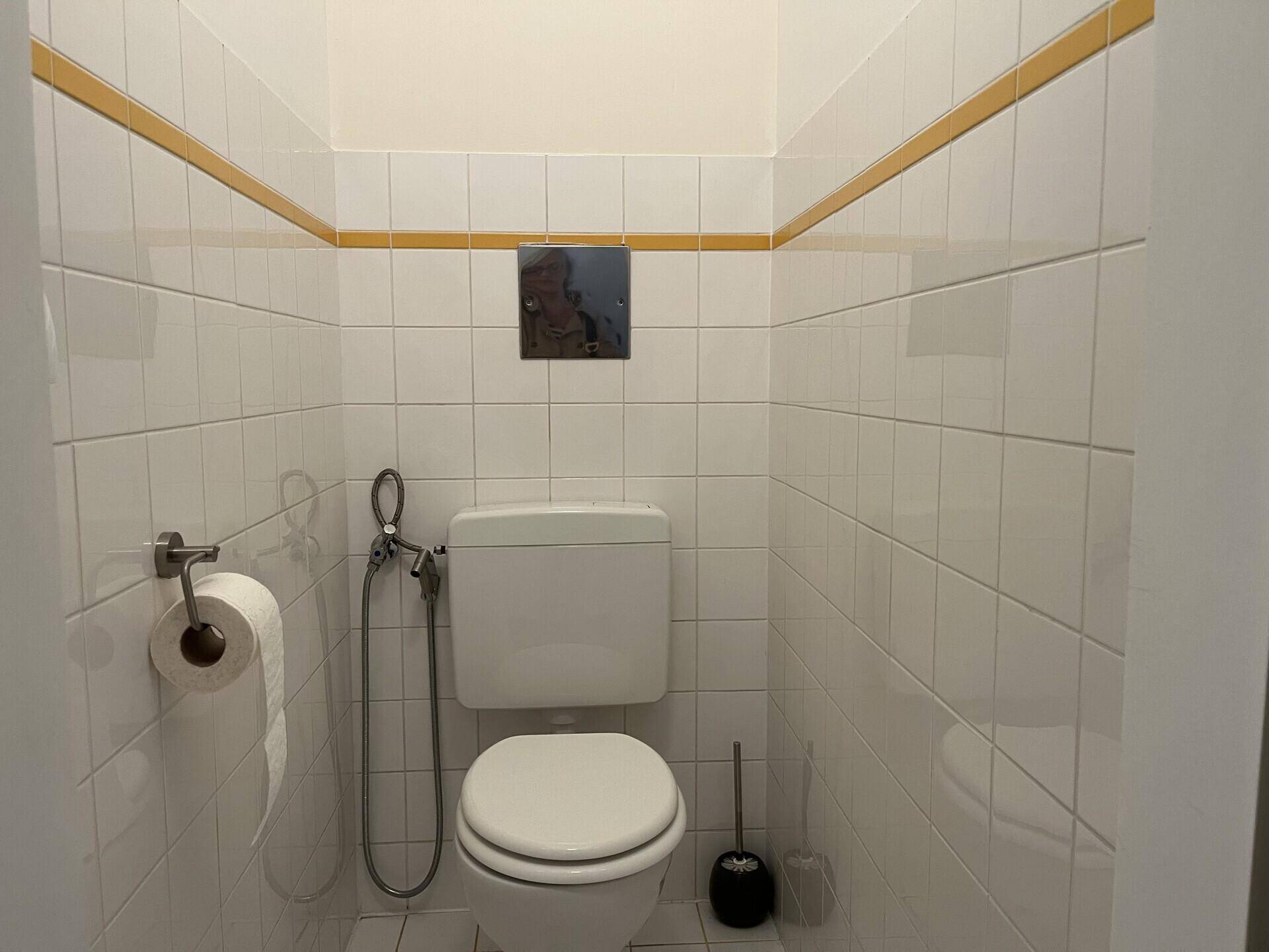 Separates WC mit Toilette und Bidet-Brause, vollständig gefliest mit gelbem Akzentstreifen.