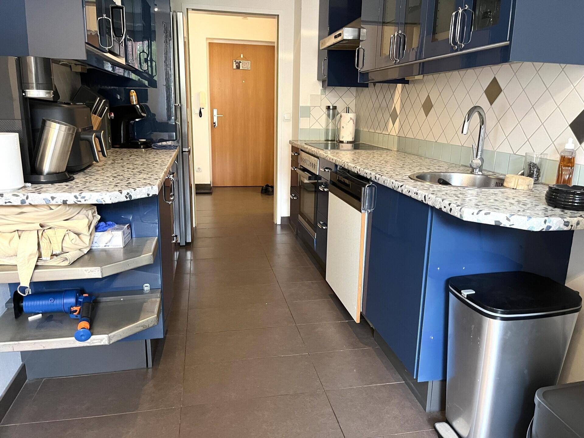 Funktionale Küche mit blauen Unterschränken, Spüle und Blick auf den Eingangsbereich der Wohnung.