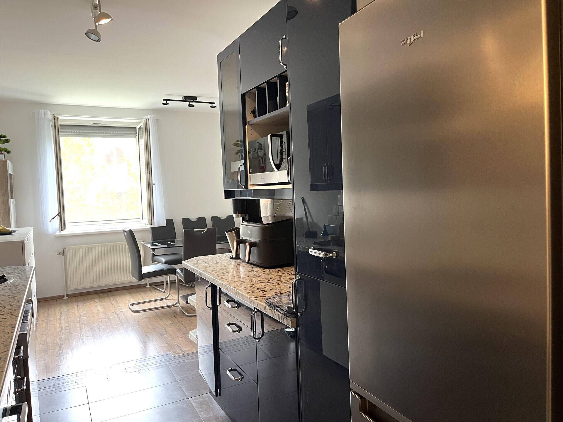 Offene Küche mit Edelstahlkühlschrank und dunklen Schränken, angrenzend an den Essbereich.