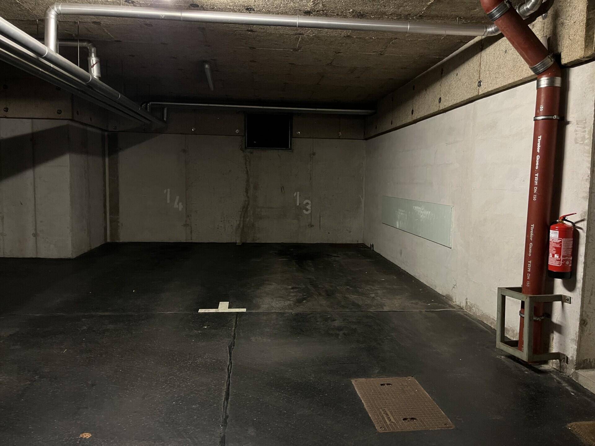 Tiefgaragenstellplatz mit sichtbaren Leitungen und einem Feuerlöscher an der Wand.