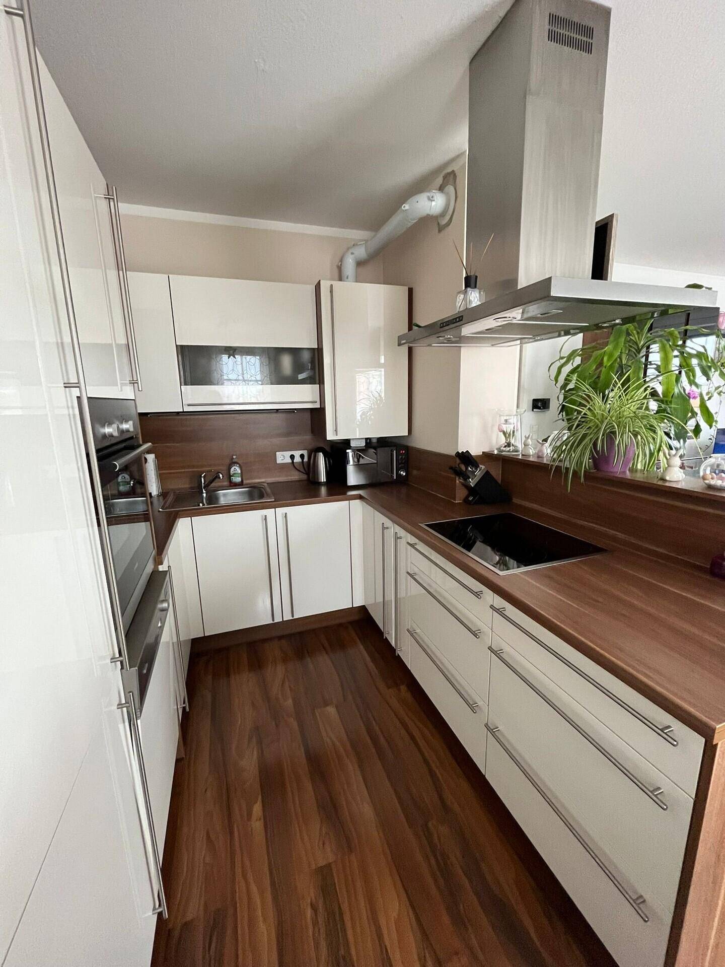 Moderne Küche mit weißen Hochglanzfronten, Holz-Arbeitsplatten und integrierten Geräten.