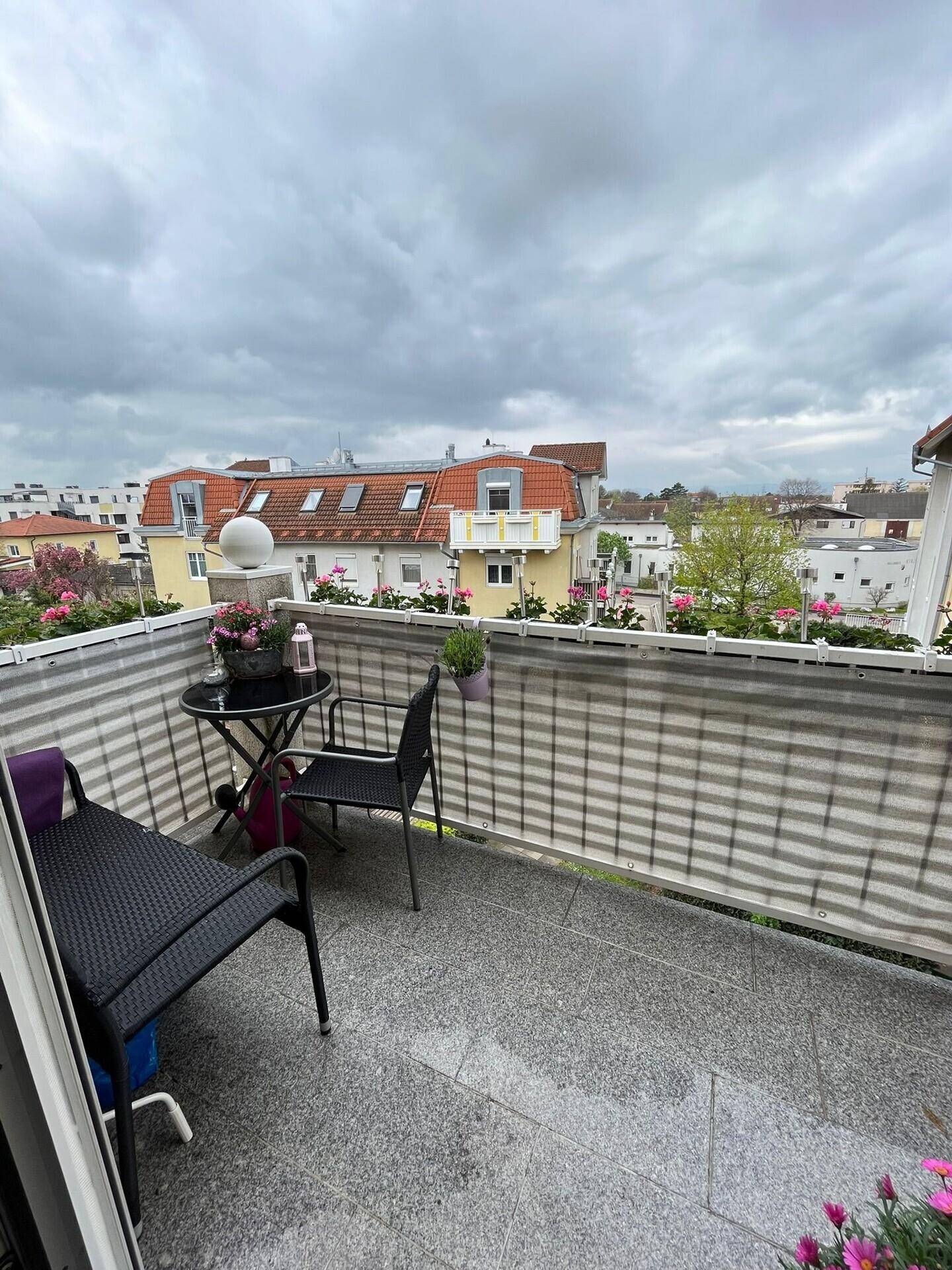 Möblierter Balkon mit Granitfliesen und Blick auf die umliegenden Dächer und Gebäude.