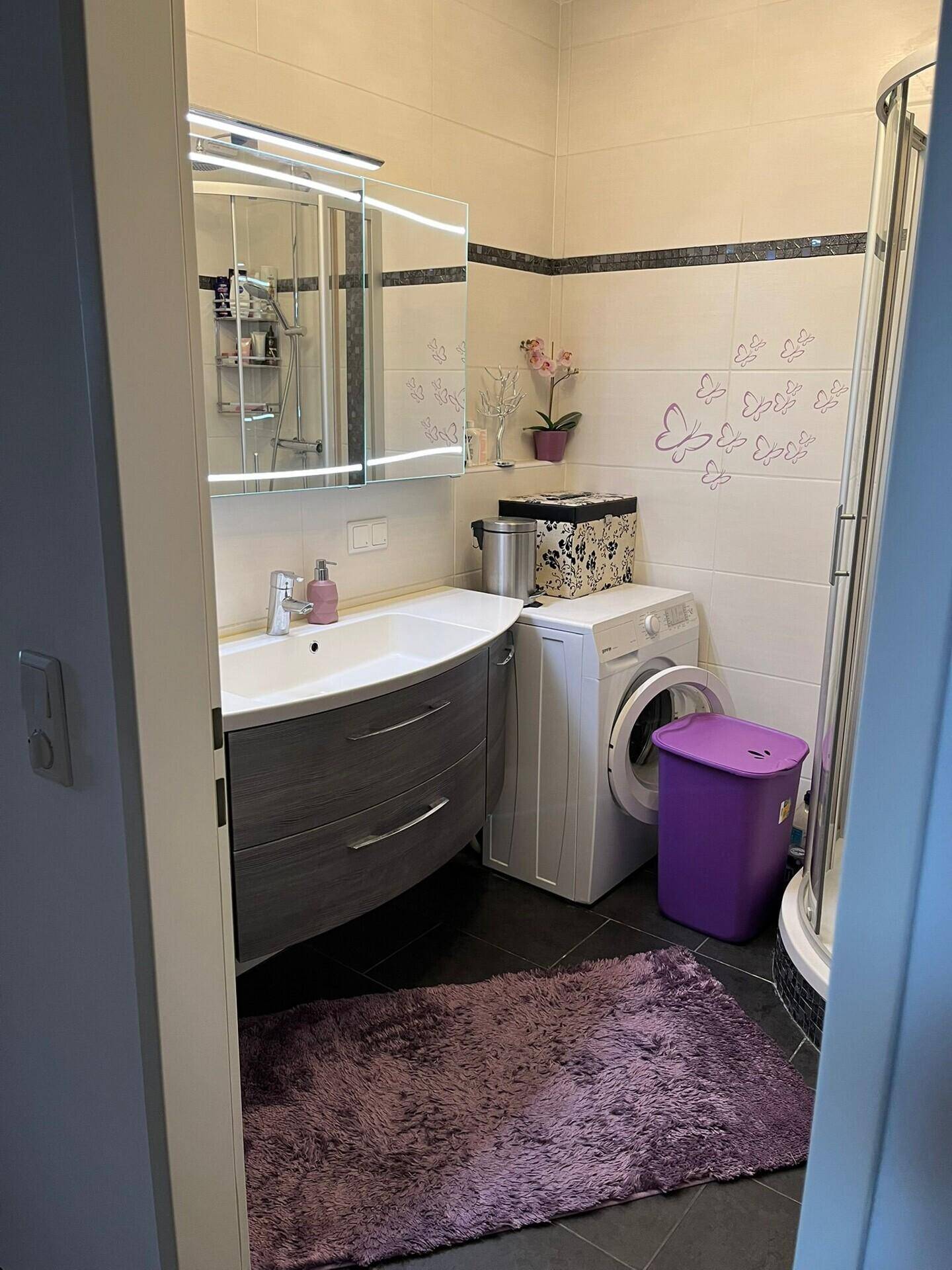 Modernes Badezimmer mit Waschbecken, Waschmaschine und Eckdusche, hell gefliest.