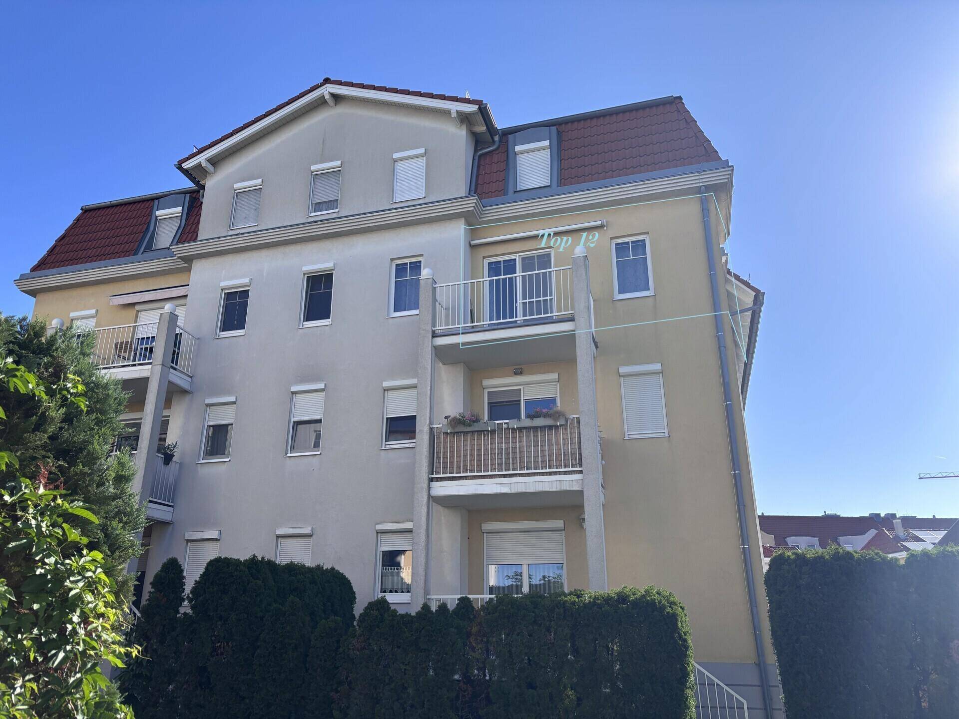 Sonnenbeschienene Fassade eines Mehrfamilienhauses mit Balkonen und roten Ziegeldächern.