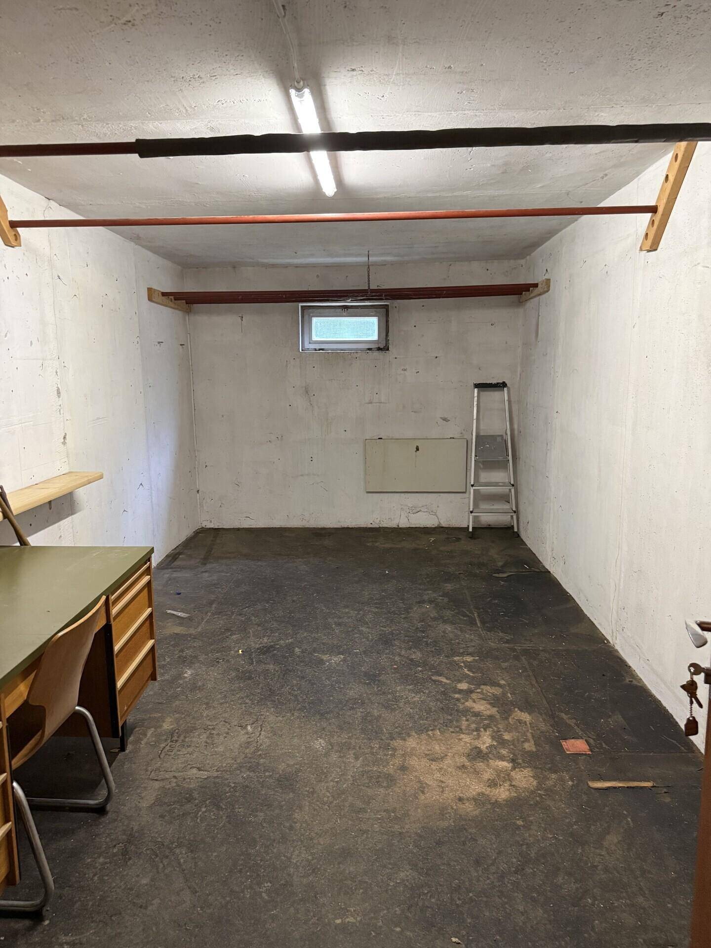 Geräumiger Kellerraum mit Betonboden, kleinem Fenster und einfacher Beleuchtung.