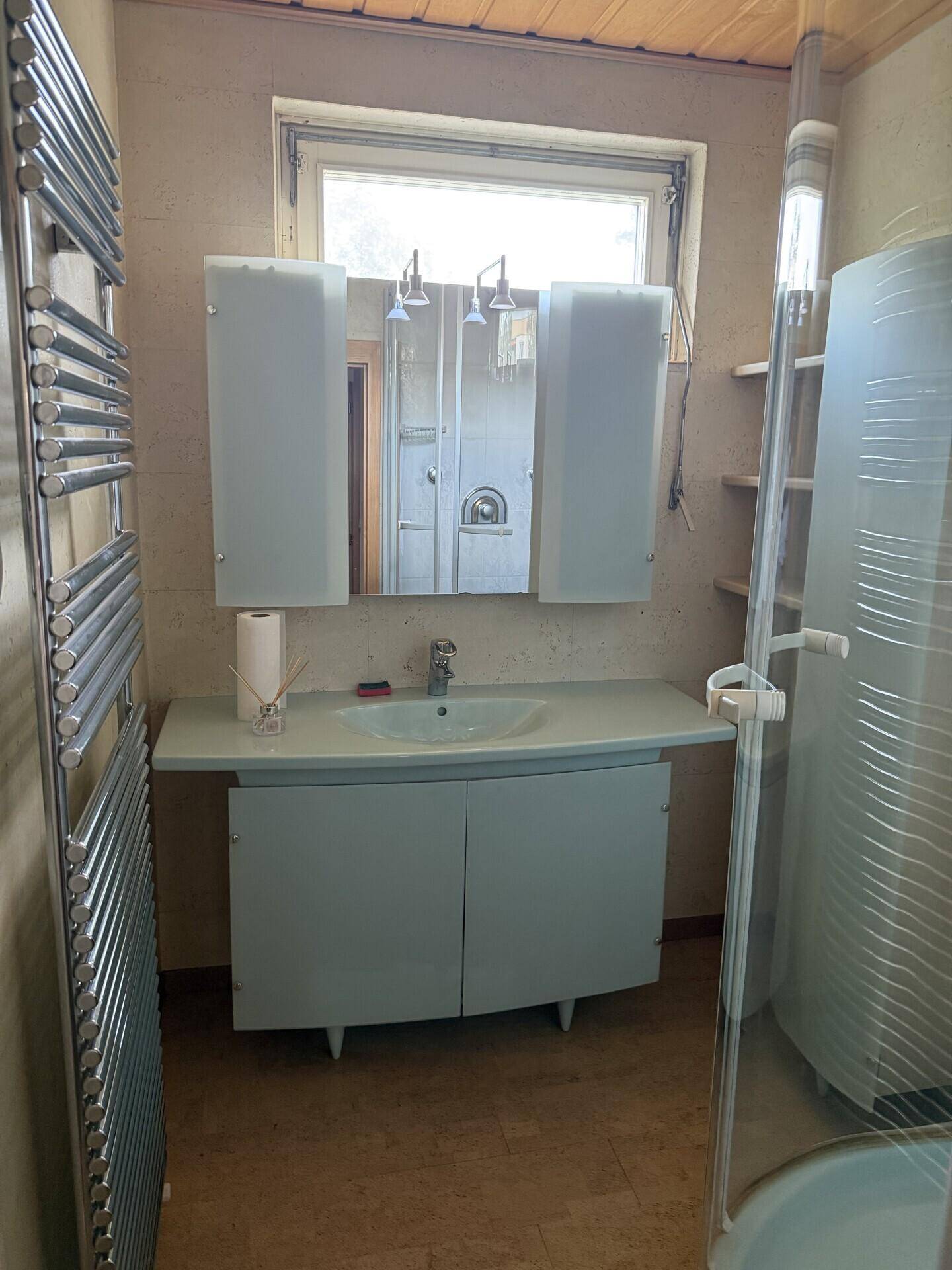 Badezimmer mit Waschbecken, Spiegelschrank, Duschkabine und Fenster.