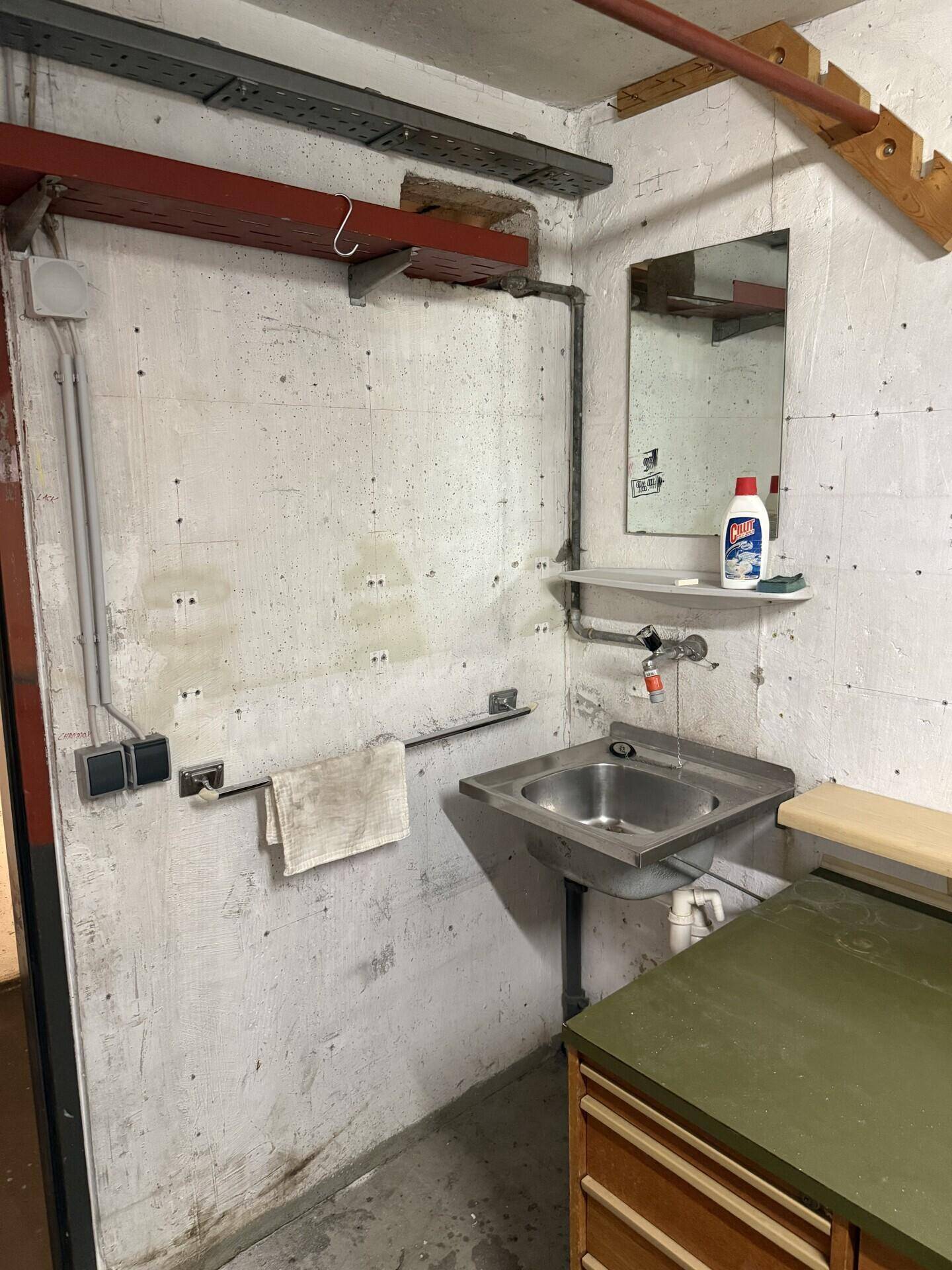 Kellerraum mit Waschbecken, Spiegel und einfacher Ausstattung, ideal als Werkstatt.
