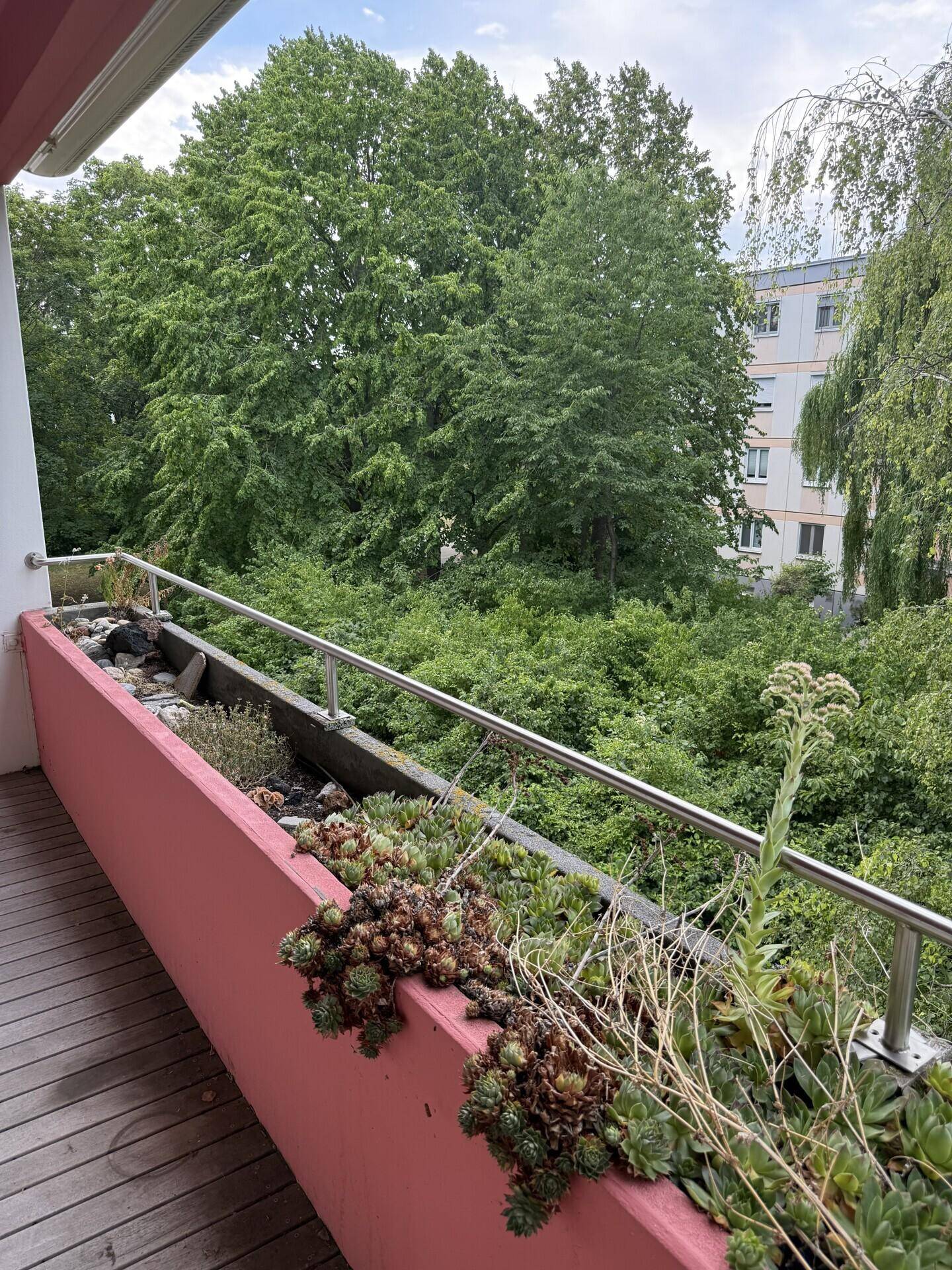 Balkon mit Holzboden und Pflanzenkübeln, bietet einen weiten Blick ins Grüne.