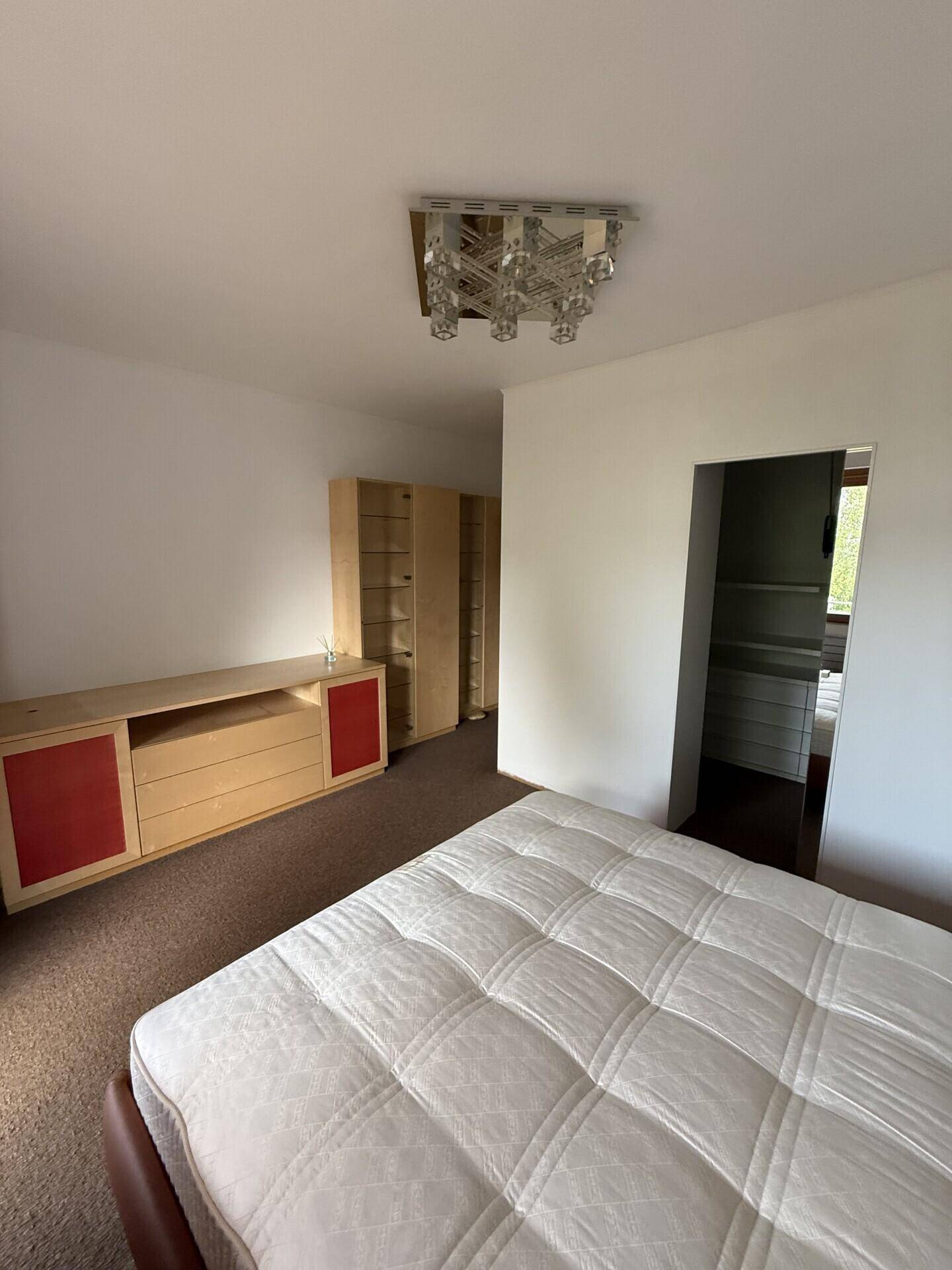 Schlafzimmer mit Teppichboden, Bett und Holzmöbeln, die Stauraum bieten.