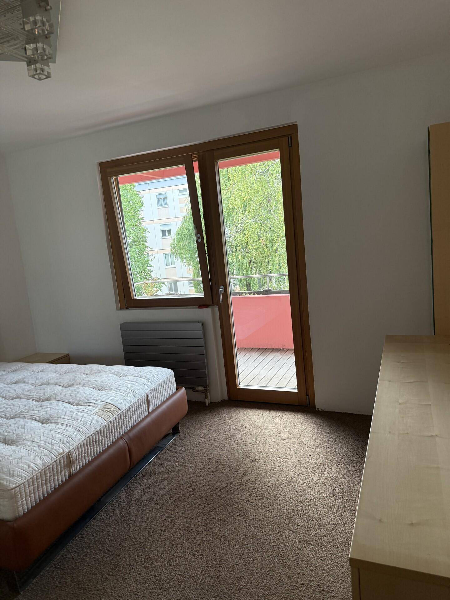 Schlafzimmer mit Teppichboden, Bett und Zugang zu einem Balkon mit Blick ins Grüne.