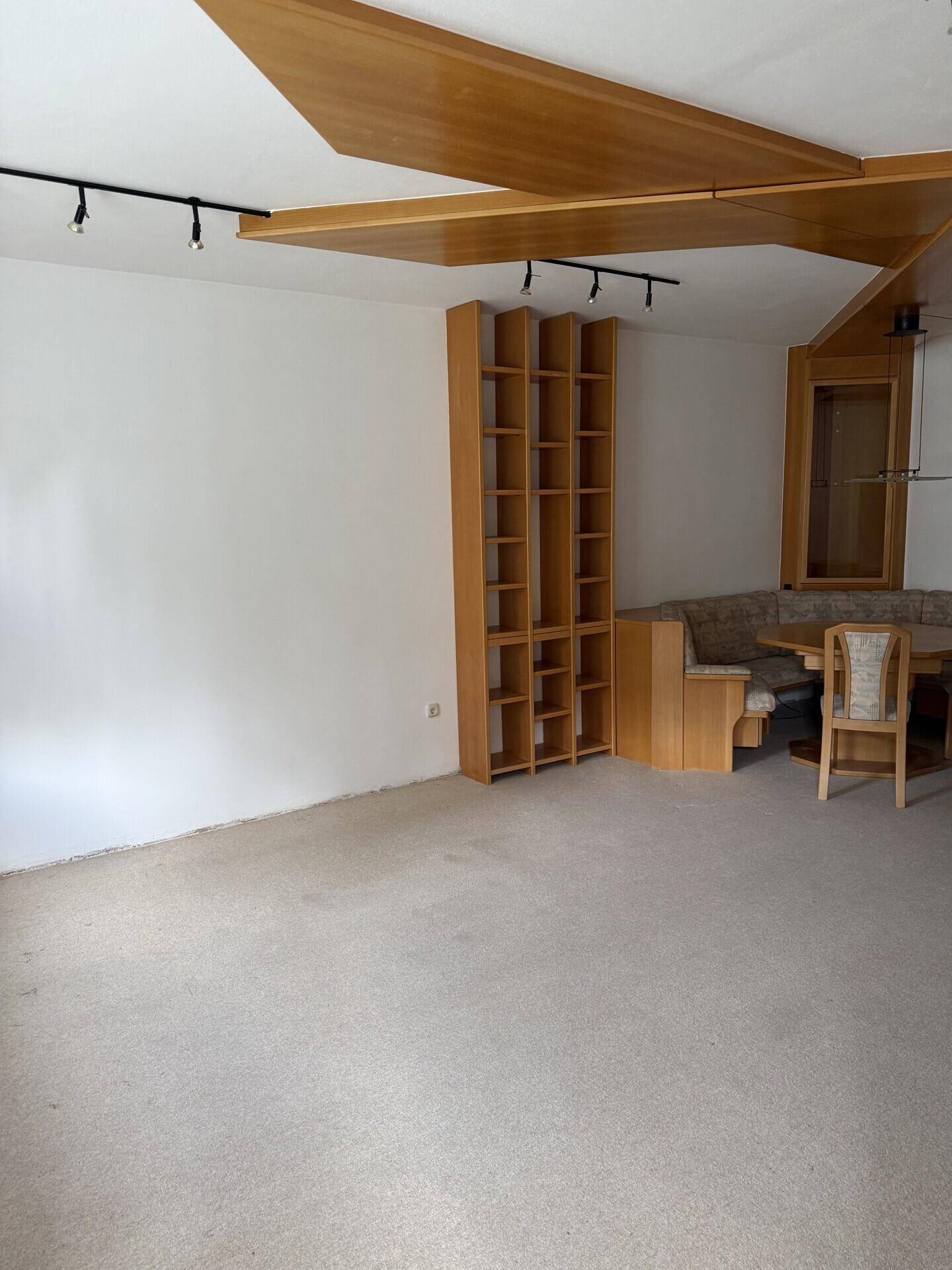 Geräumiger Wohn-Essbereich mit Teppichboden, Holzelementen an der Decke und Einbauregalen.