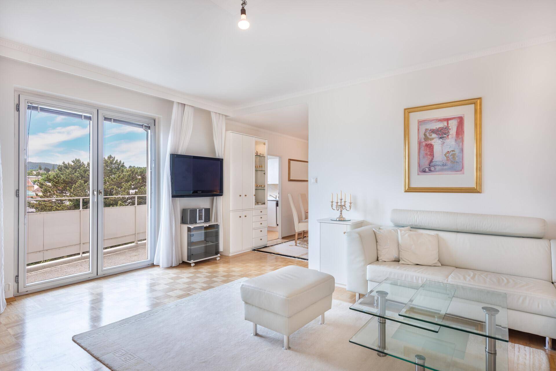 Helles Wohnzimmer mit weißem Sofa, Glas-Couchtisch und Zugang zu einem sonnigen Balkon.