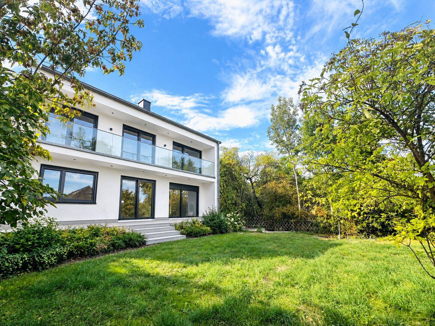 Rückseite eines modernen Hauses mit Balkonen und einem gepflegten Rasenbereich im Garten.